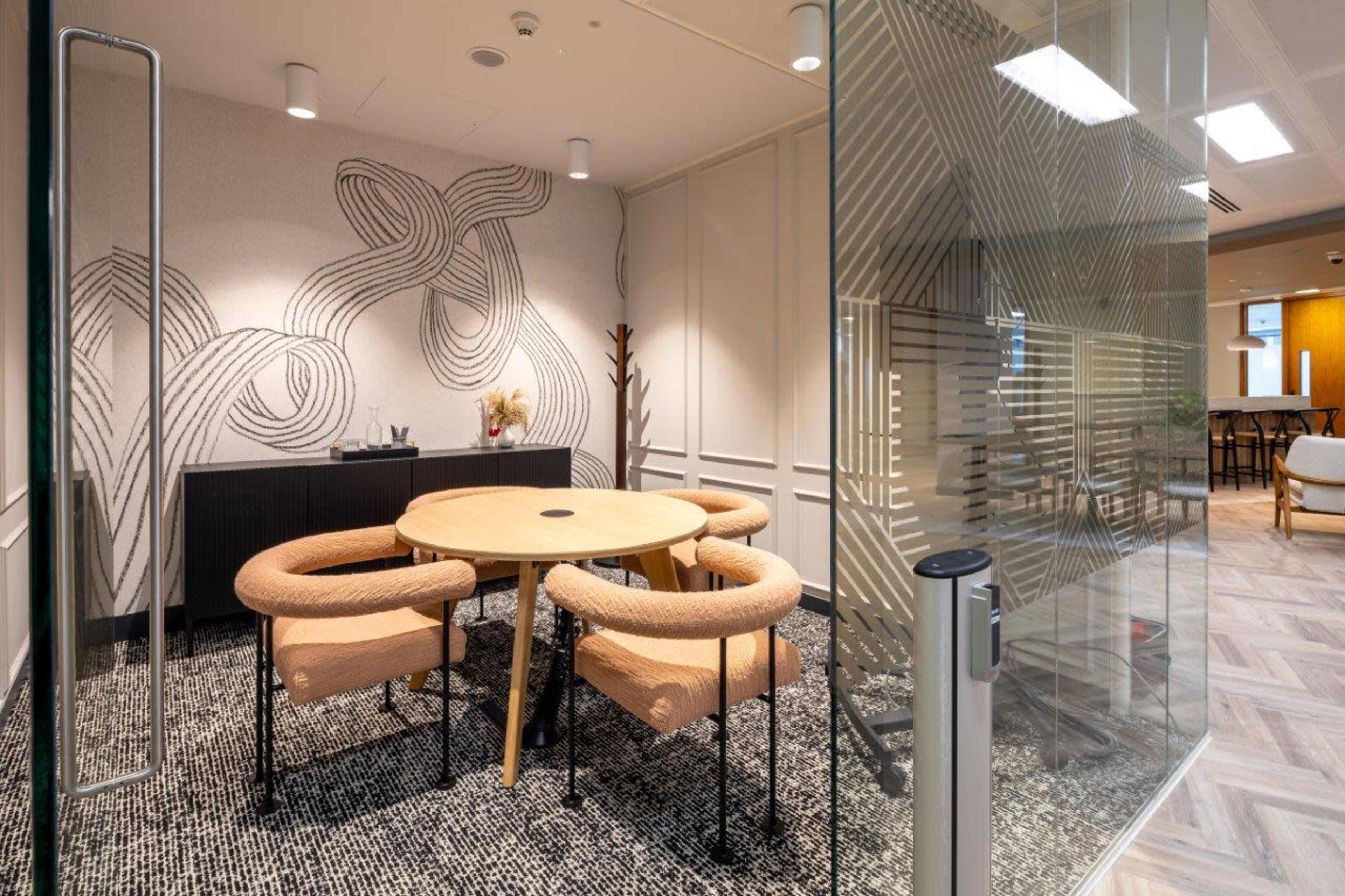 A small meeting room features a round table surrounded by four cushioned chairs, with a patterned wall design and a textured floor.