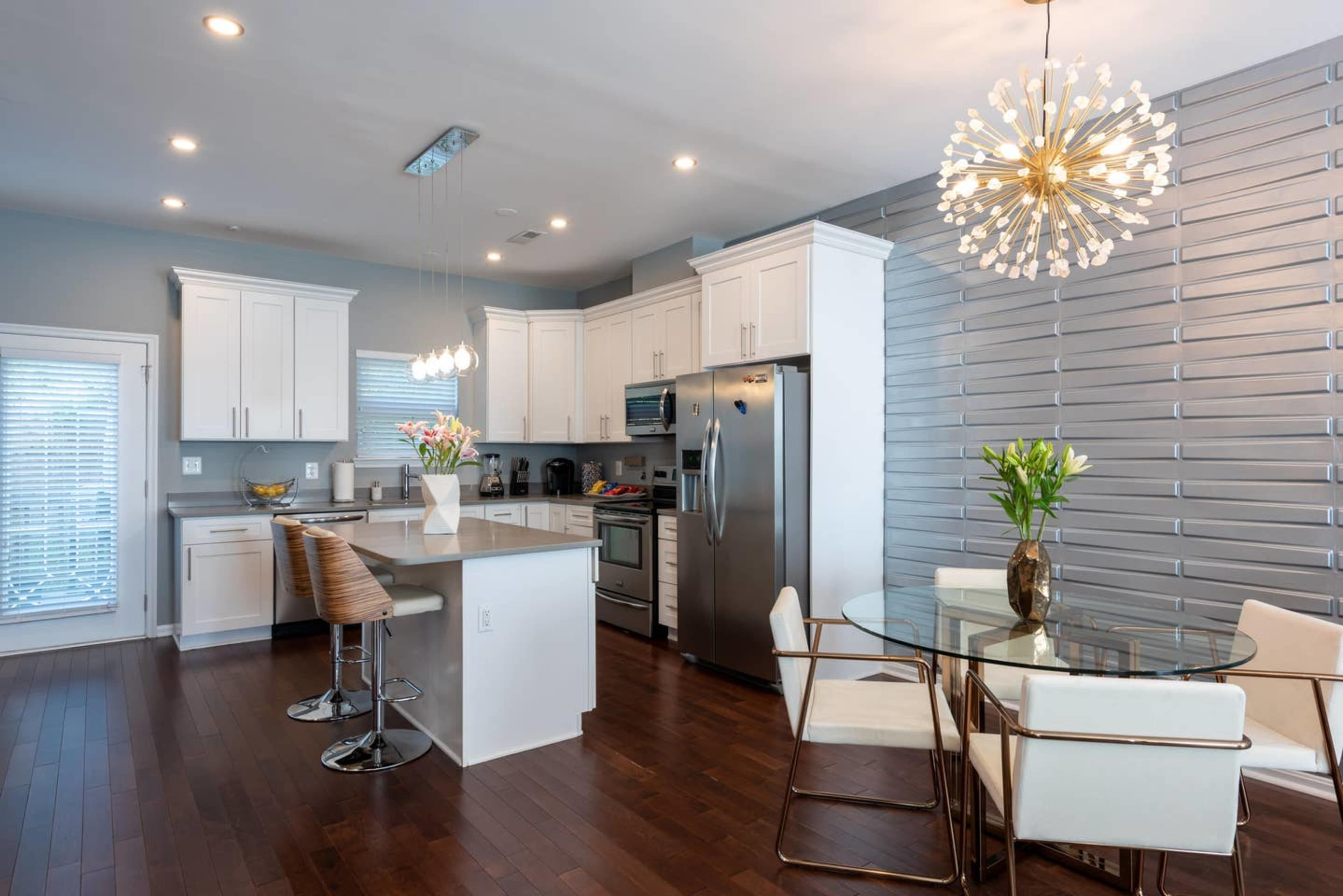 A modern kitchen with white cabinets, stainless steel appliances, and a dining area featuring a glass table and four chairs.