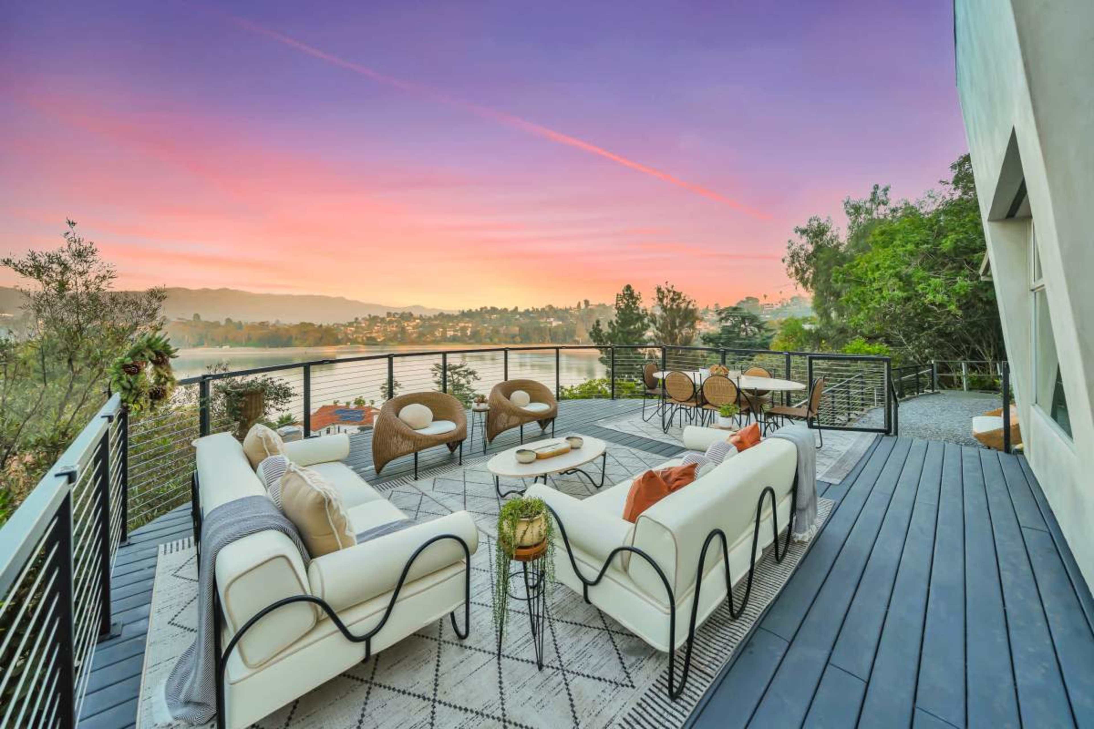 A modern deck features stylish outdoor furniture and offers a view of a lake at sunset.