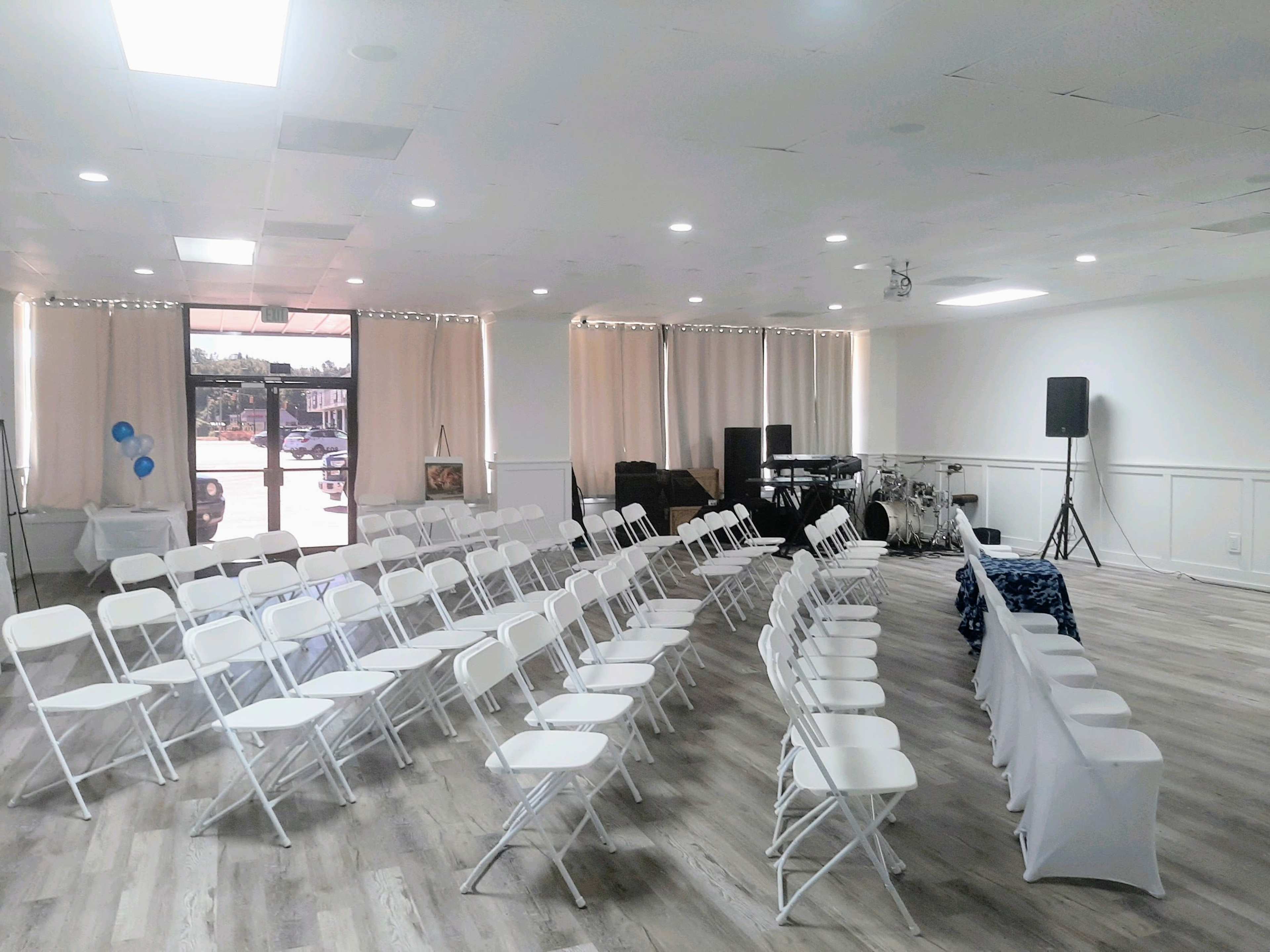 A spacious room set up with rows of white folding chairs facing a stage area with a band setup and decorative elements.
