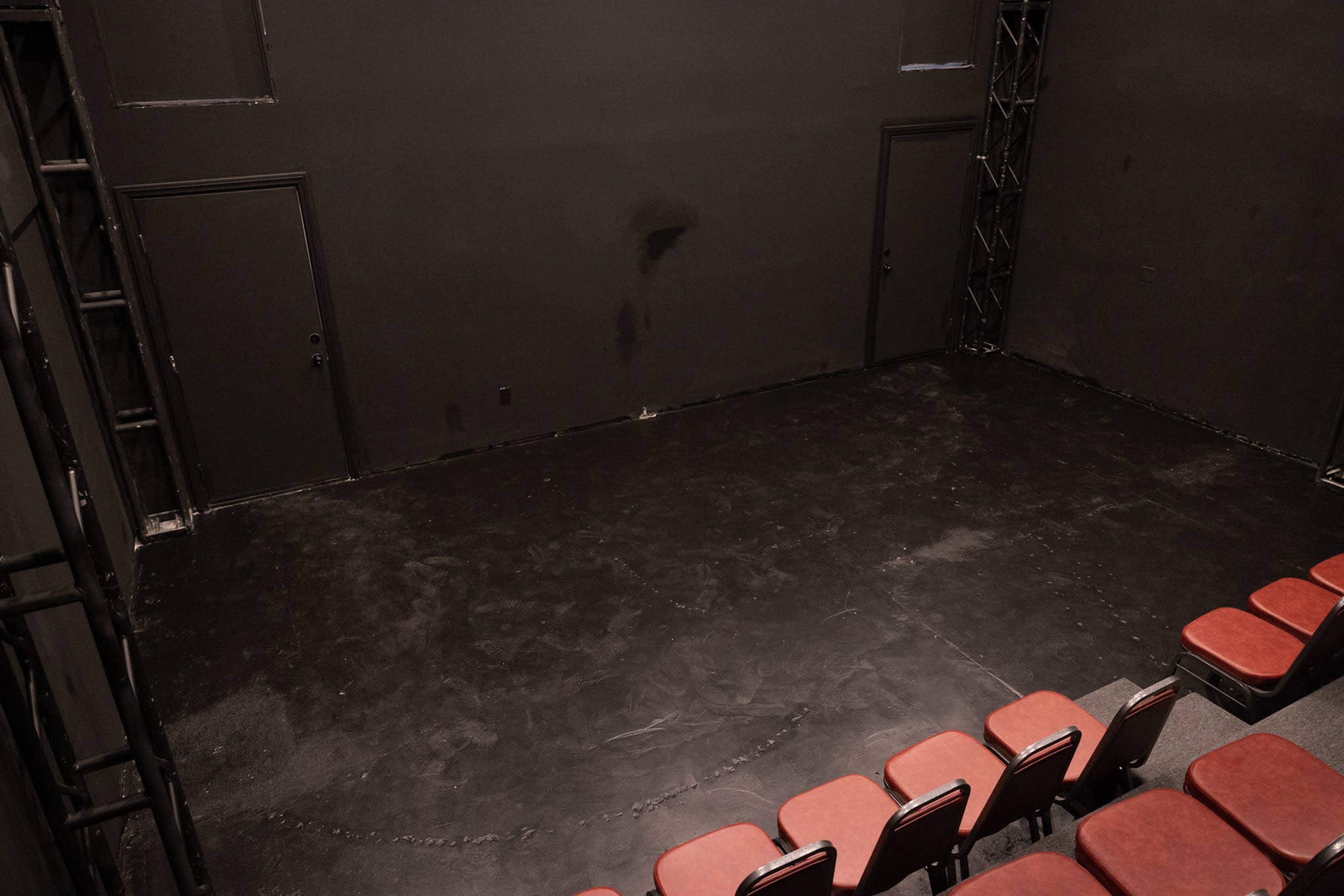 A sparsely furnished black box theater with red chairs arranged in a semicircle facing a bare stage area.