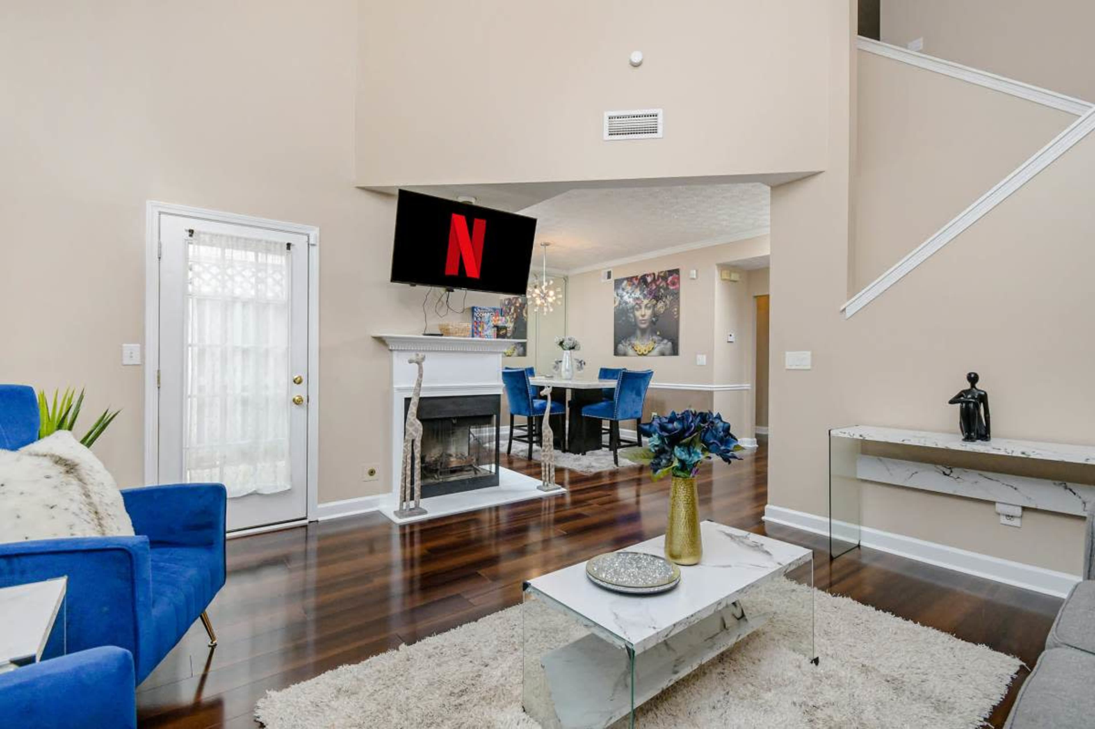The living room features a fireplace, a large television mounted on the wall, and a seating area with blue chairs and a coffee table.