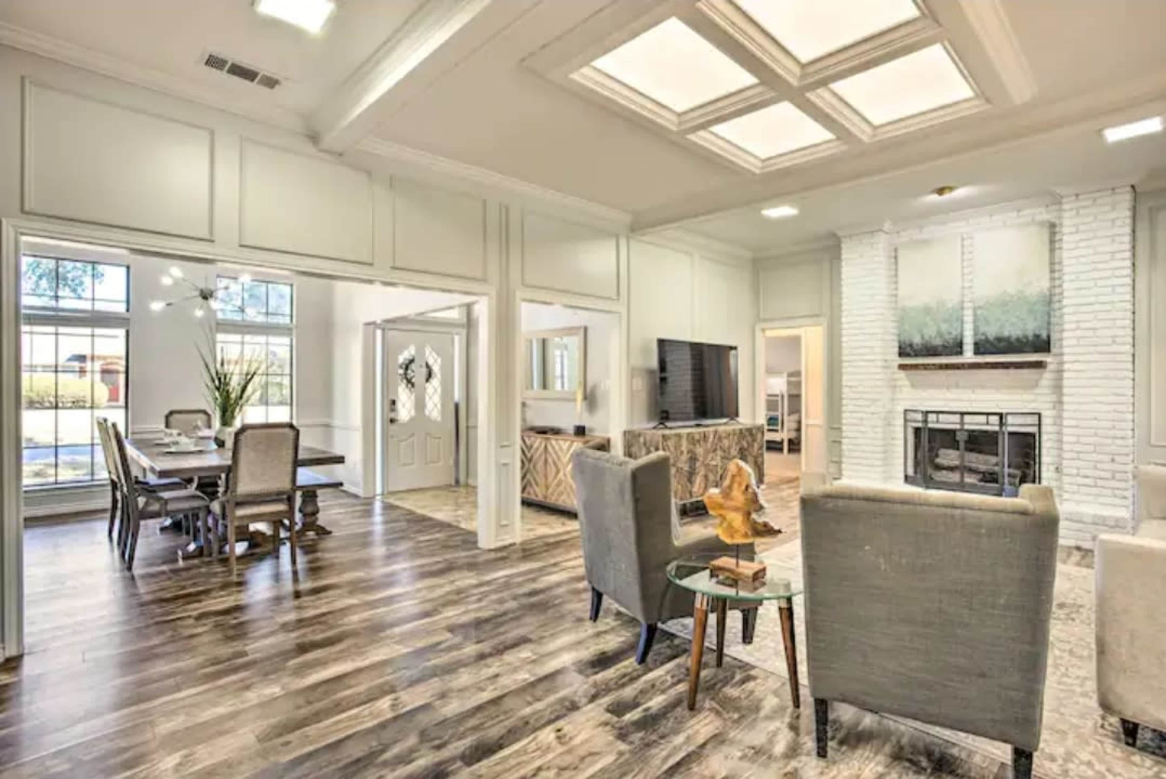 A spacious living area with wooden flooring, a seating area, and an adjacent dining space, featuring large windows and a fireplace.