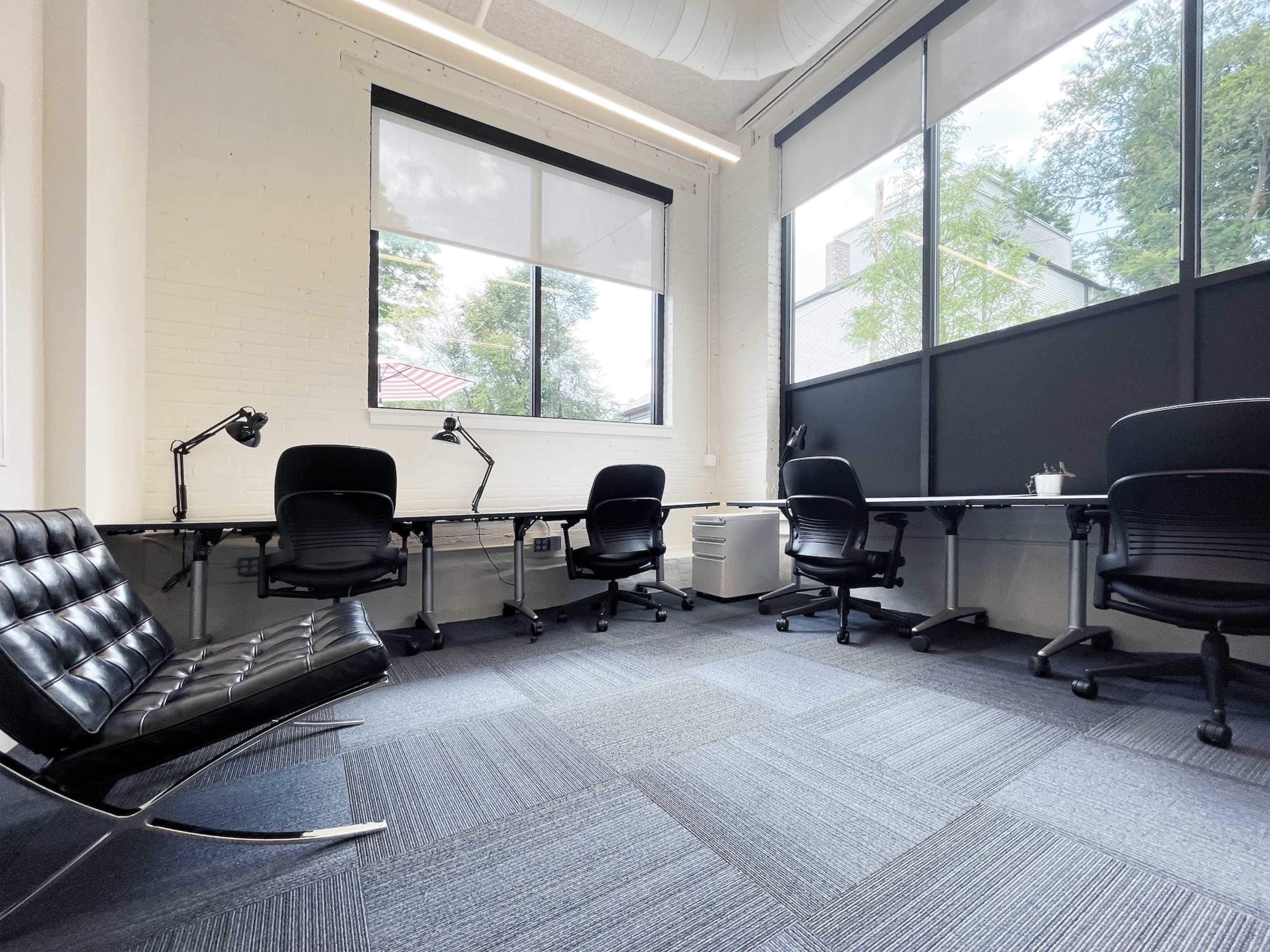 A modern office space with several chairs and desks arranged near large windows.