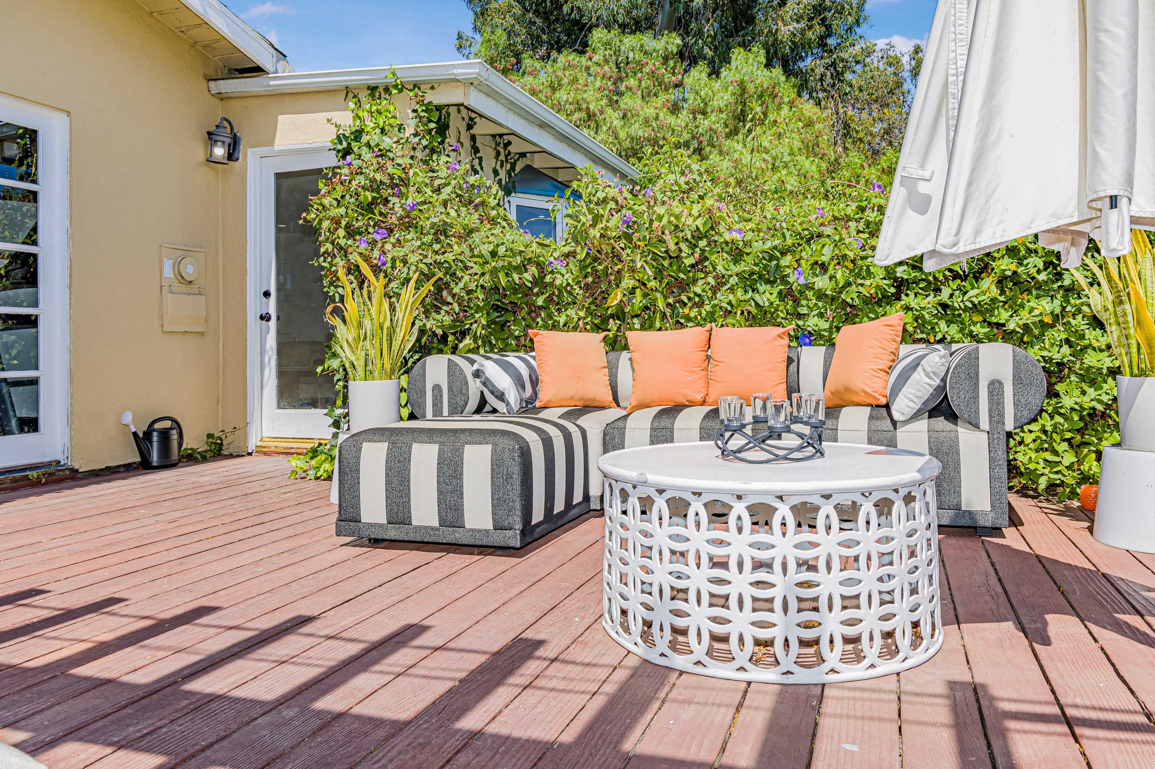 A patio area features a striped outdoor seating arrangement with orange cushions and a round, white coffee table surrounded by greenery.