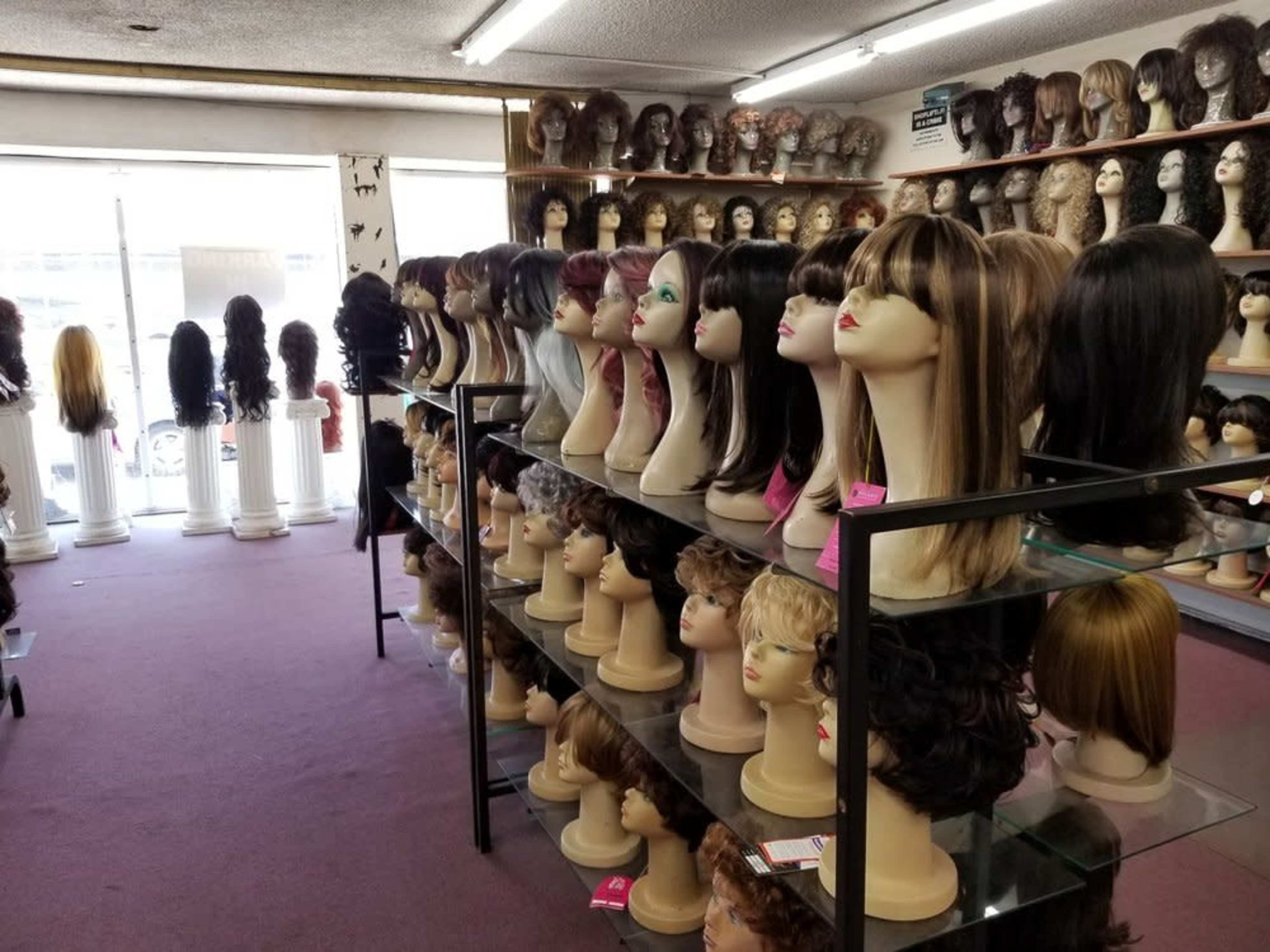 A well-organized wig store displays various styles of wigs on mannequin heads and shelves throughout the room.