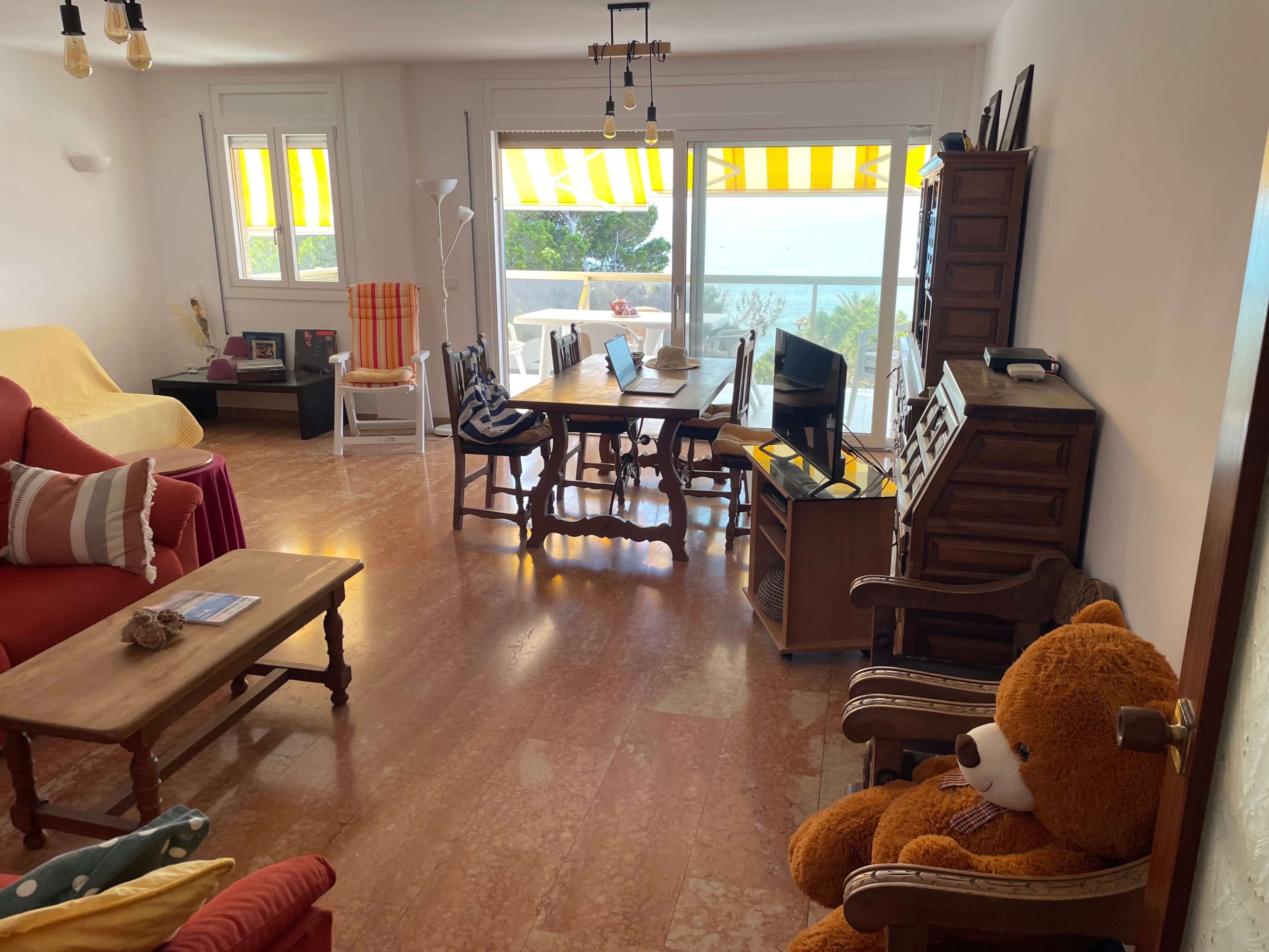 The image shows a partially furnished living room with two sofas, a dining table, and large windows overlooking a view of the outdoors.