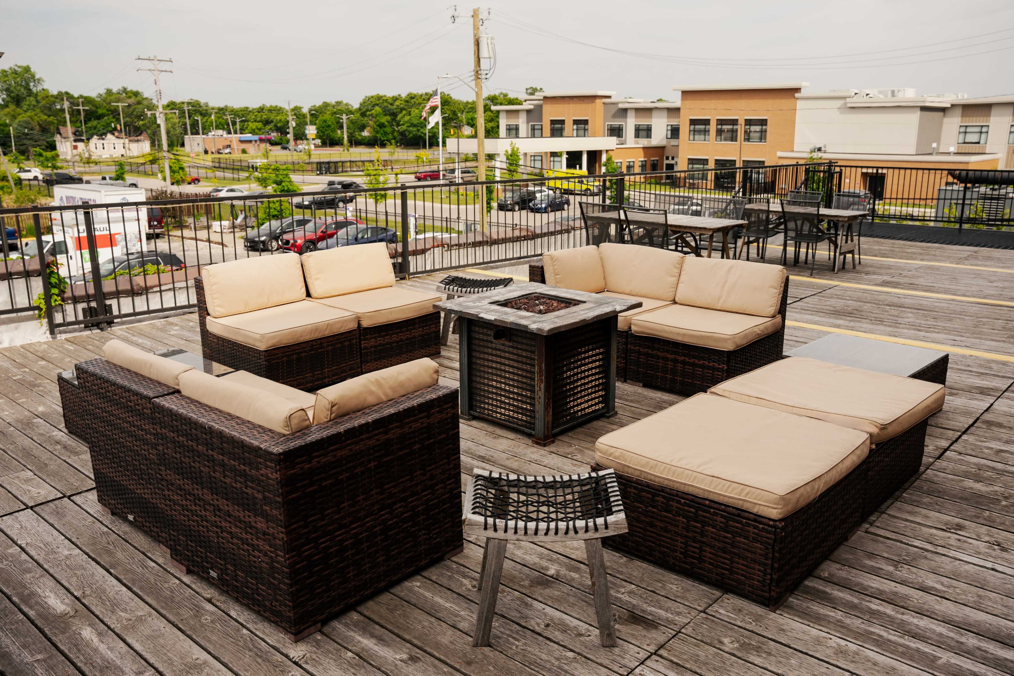 A patio area features a seating arrangement of wicker furniture with cream-colored cushions surrounding a small fire pit.