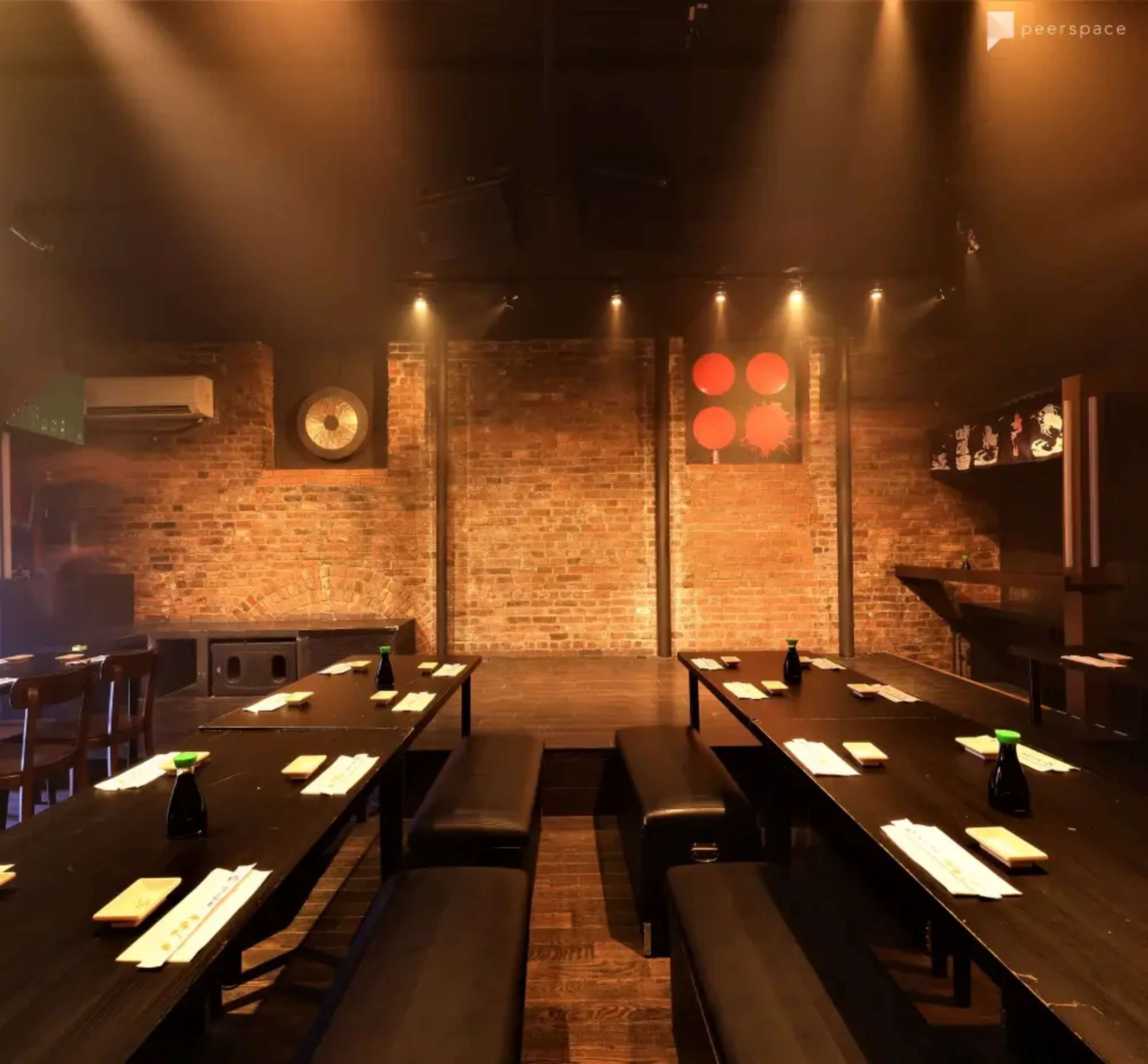 The image shows a dimly lit restaurant interior with long tables, benches, and exposed brick walls.