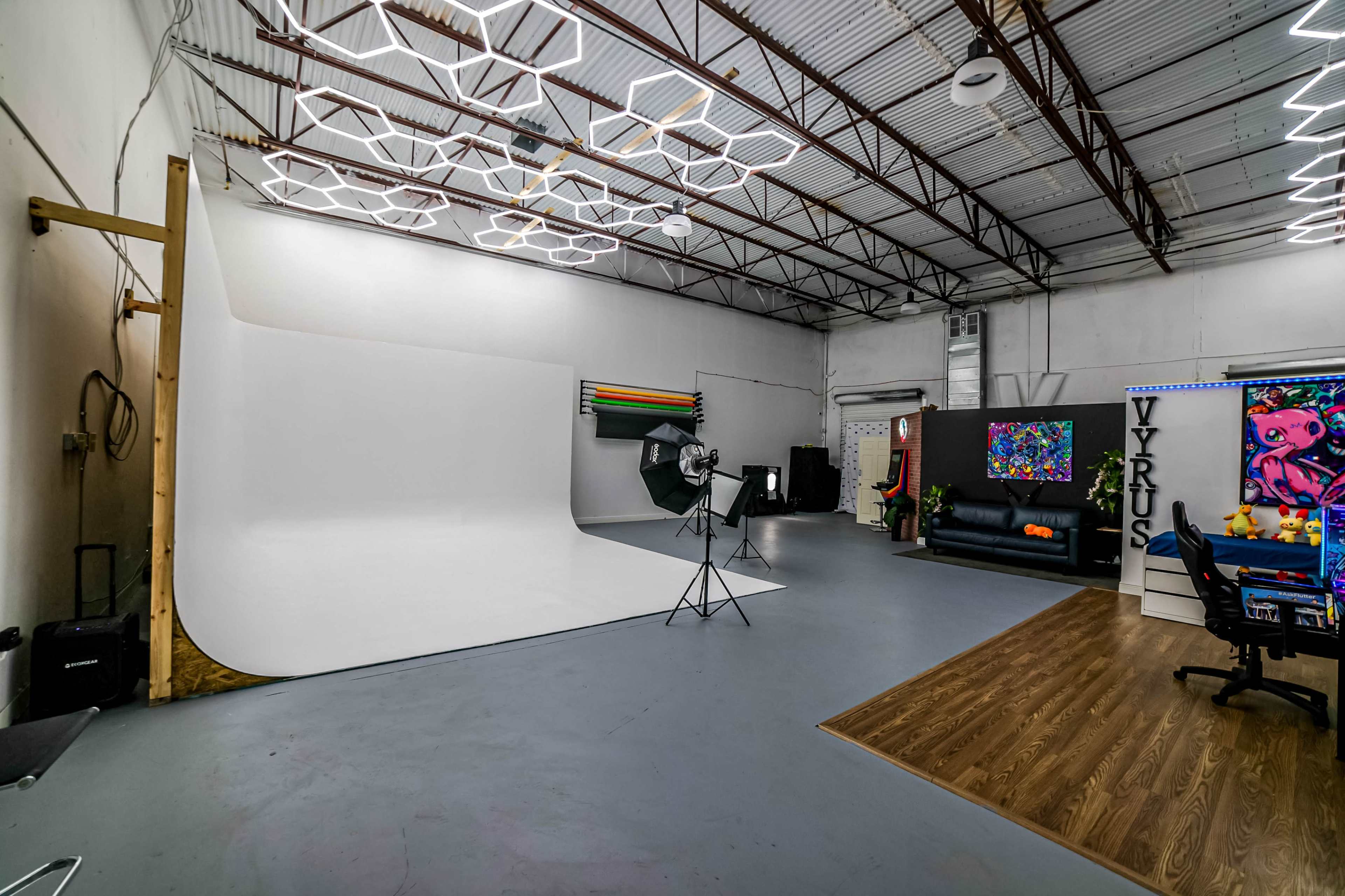 A spacious studio with a white backdrop, photography equipment, and modern furnishings including a black couch and colorful artwork.