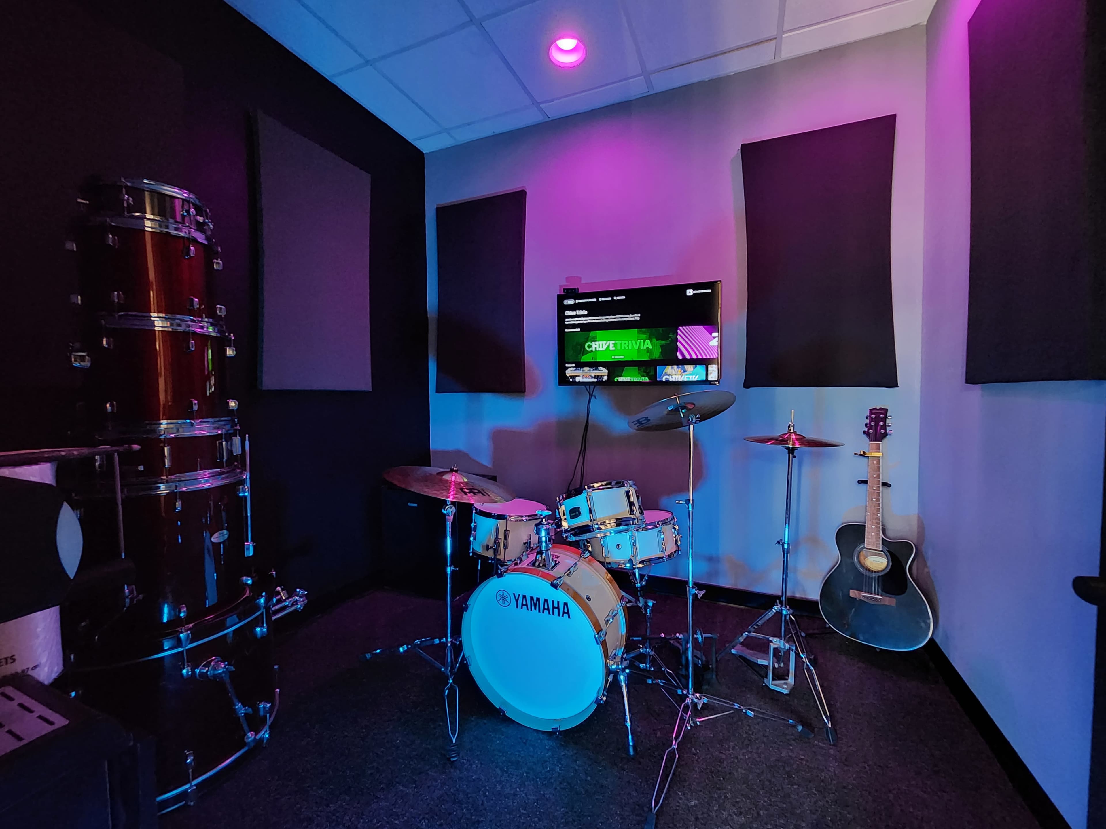 A music practice room featuring a Yamaha drum set, an electric guitar, and colorful lighting.