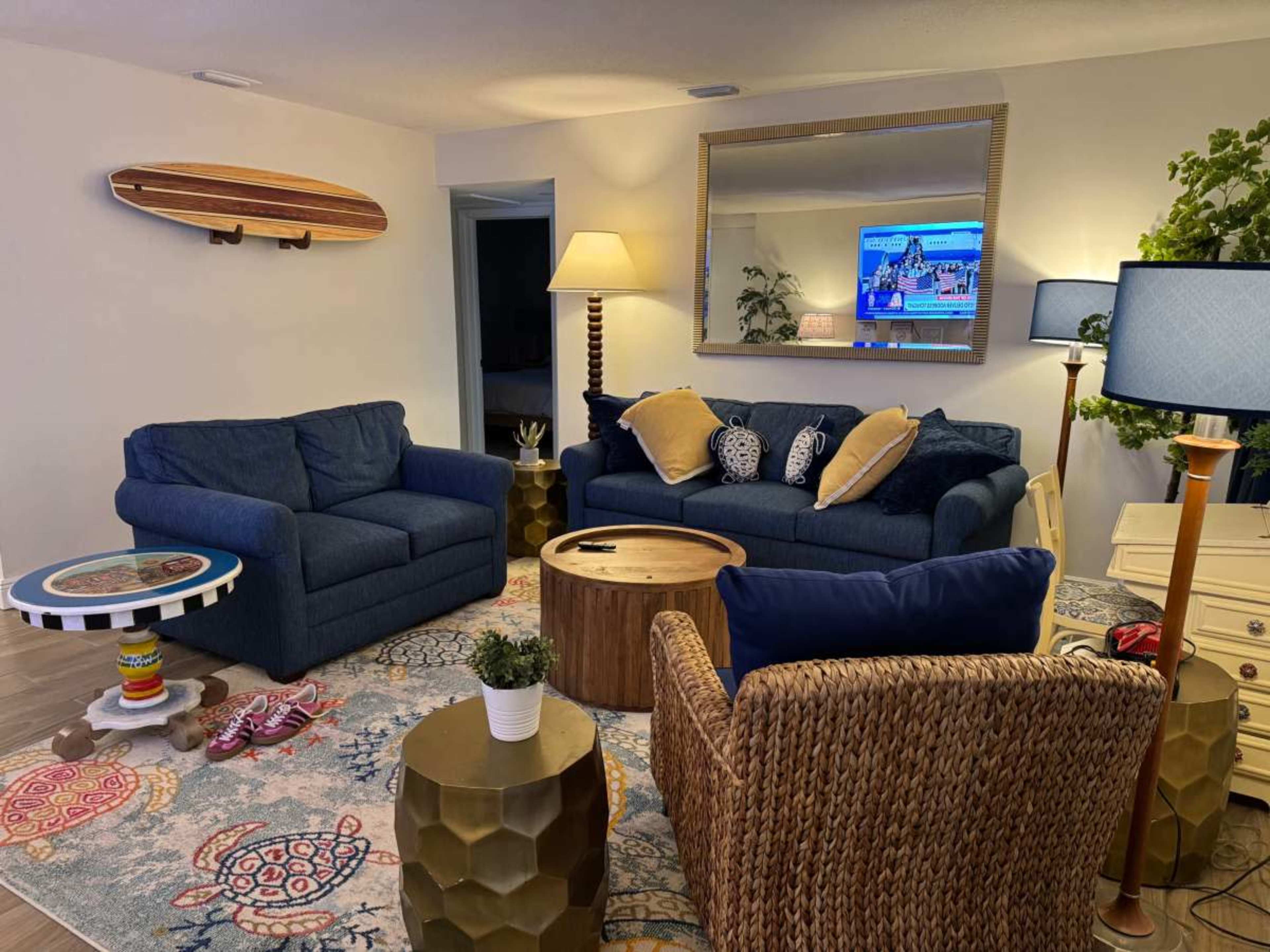 The image shows a cozy living room featuring a blue sofa set, a wooden coffee table, a decorative rug, and a television mounted on the wall.