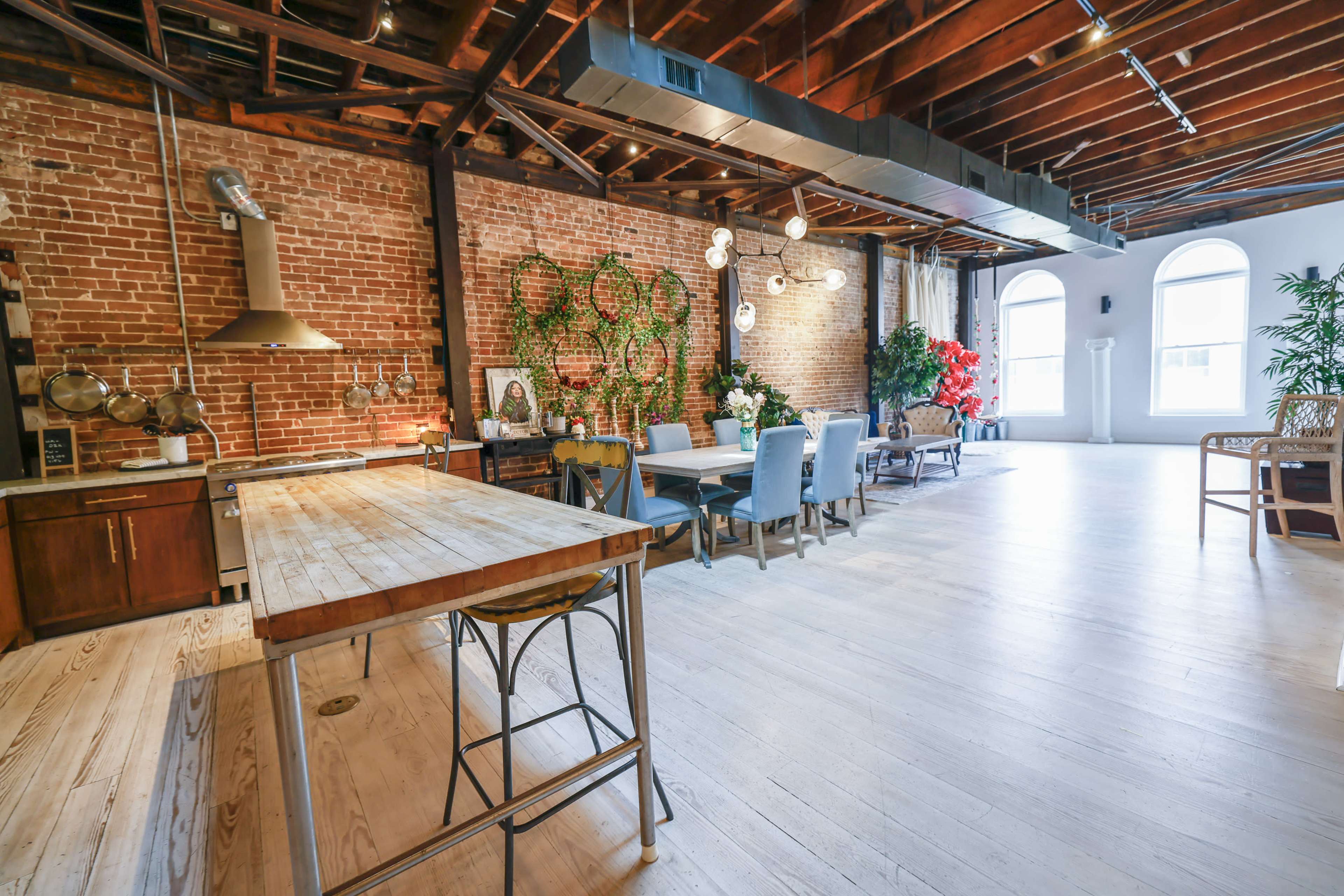 A spacious, rustic kitchen and dining area with exposed brick walls, wooden beams, and a large wooden dining table surrounded by various seating options.