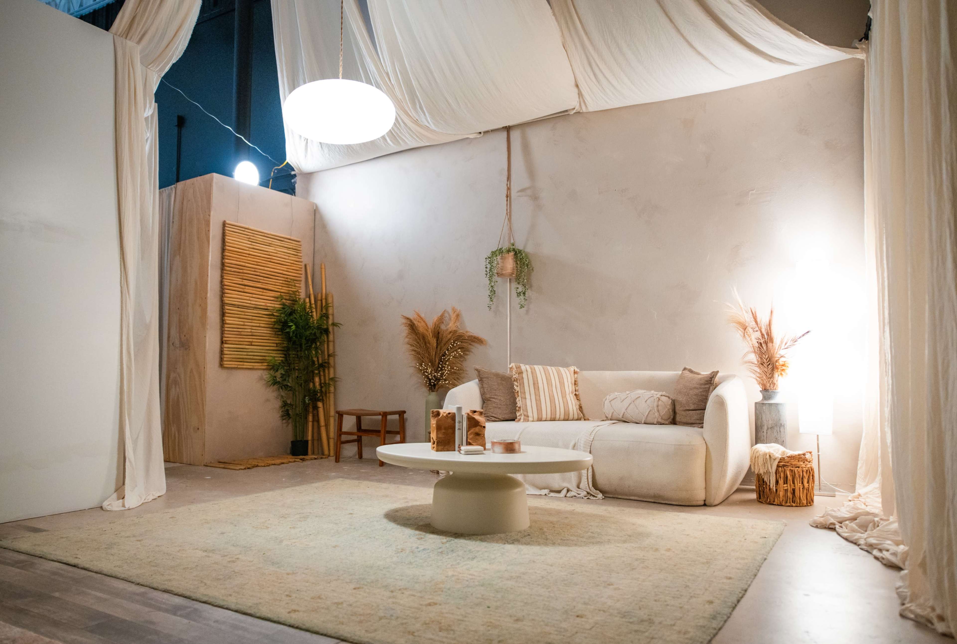 The image shows a modern, minimalist living space featuring a white sofa, a circular coffee table, and decorative plants against a softly lit backdrop.