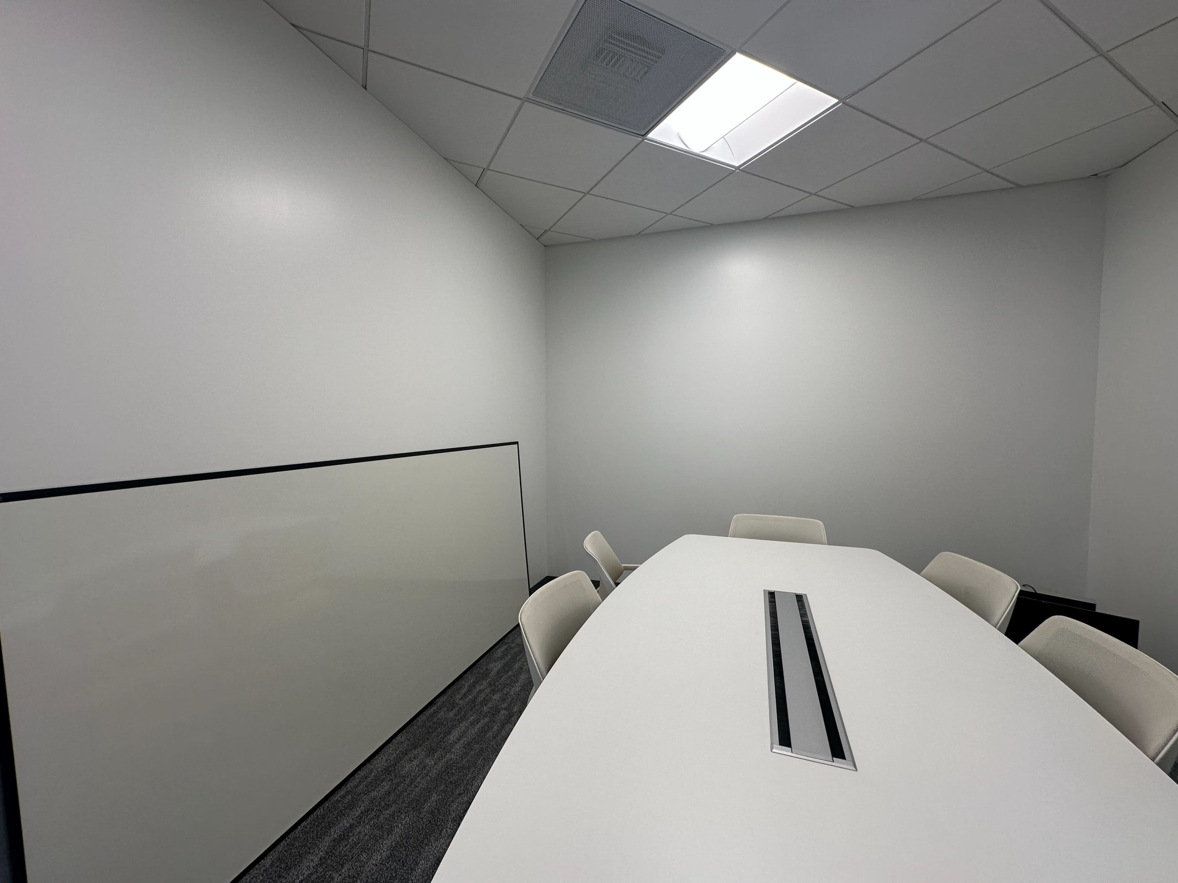 The image shows a modern conference room with a large, oval table surrounded by white chairs and a blank whiteboard on the wall.