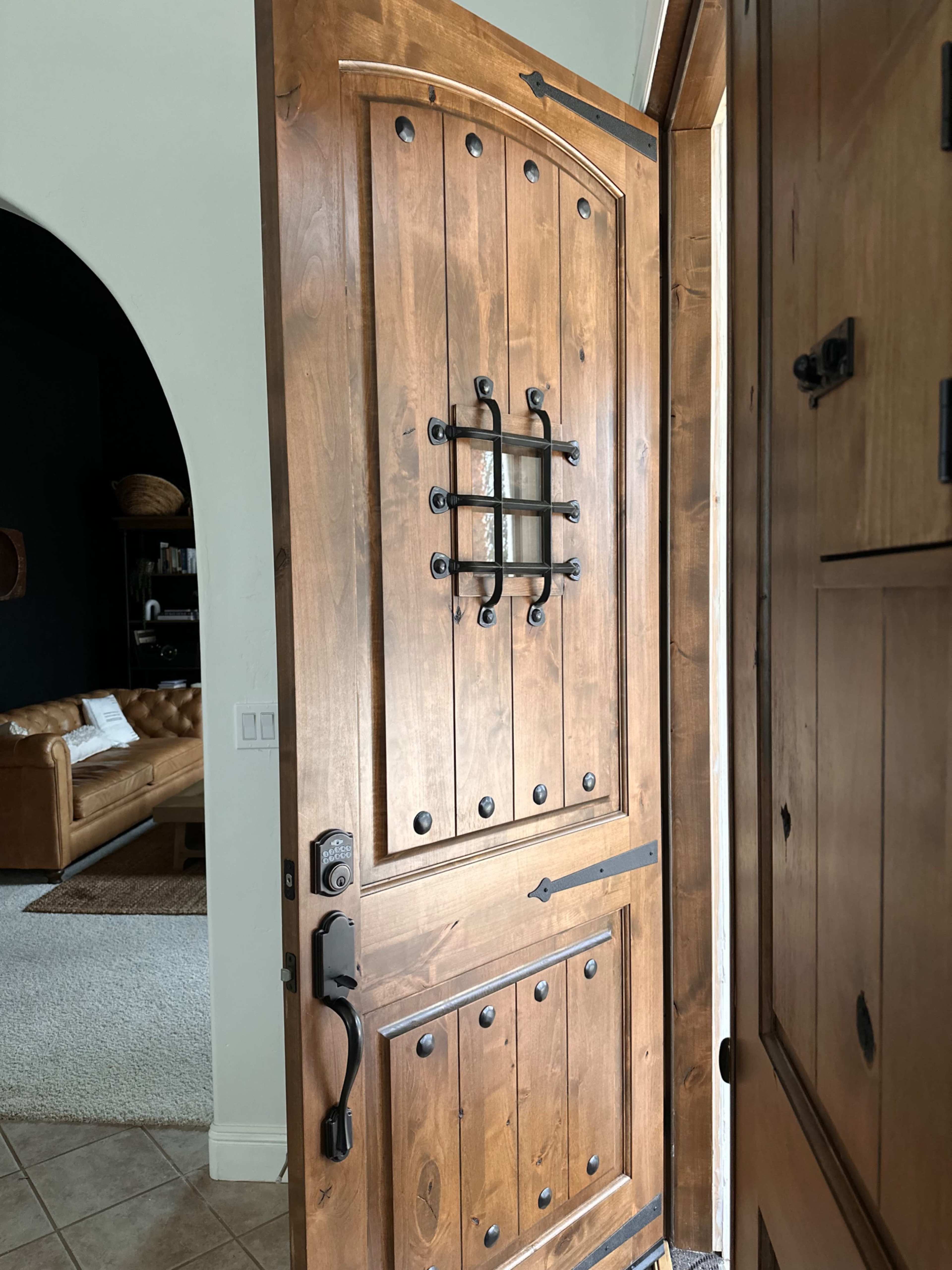 A wooden front door with a decorative grill and a nearby archway leading into a living area.