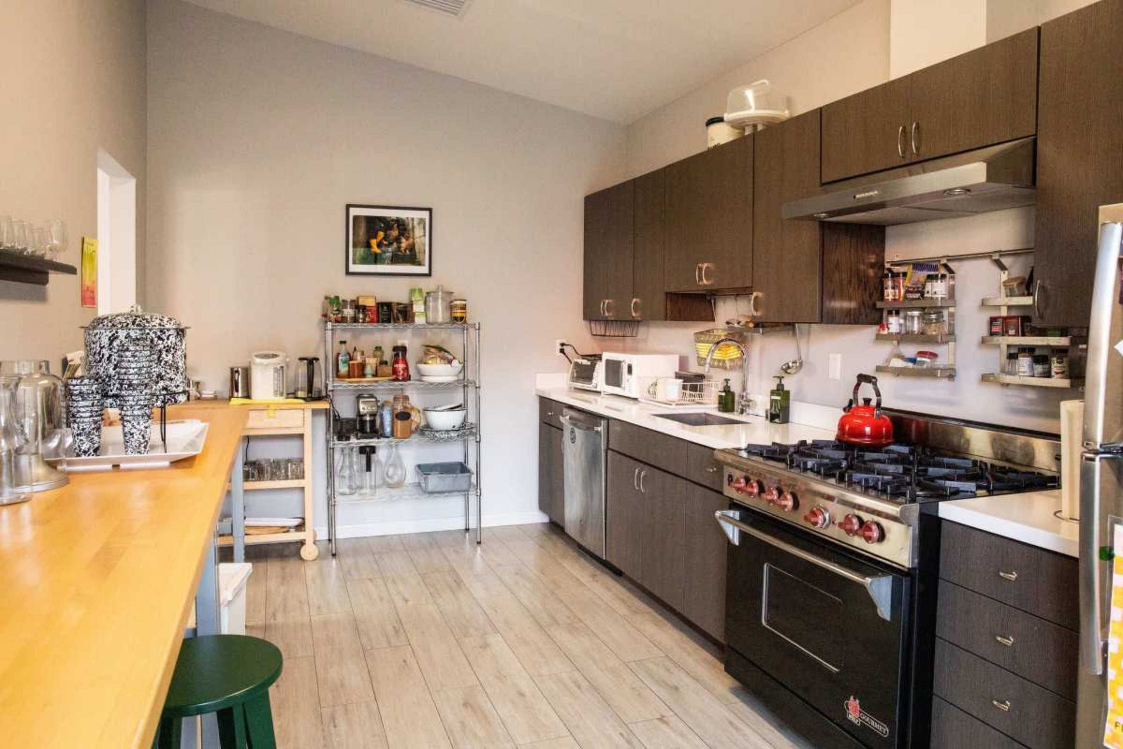 The image shows a modern kitchen equipped with dark cabinetry, a stainless steel stove, and a variety of kitchen appliances and utensils organized along the countertops.