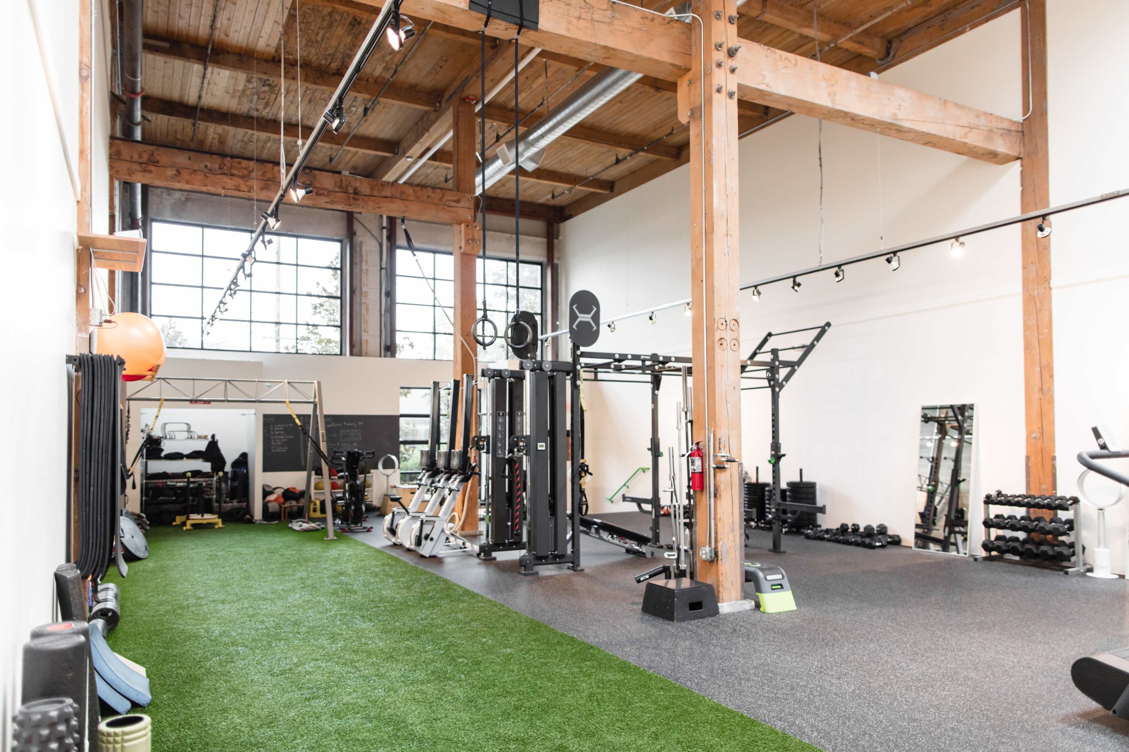 A spacious gym with wooden beams, equipped with various exercise machines, free weights, and turf flooring.