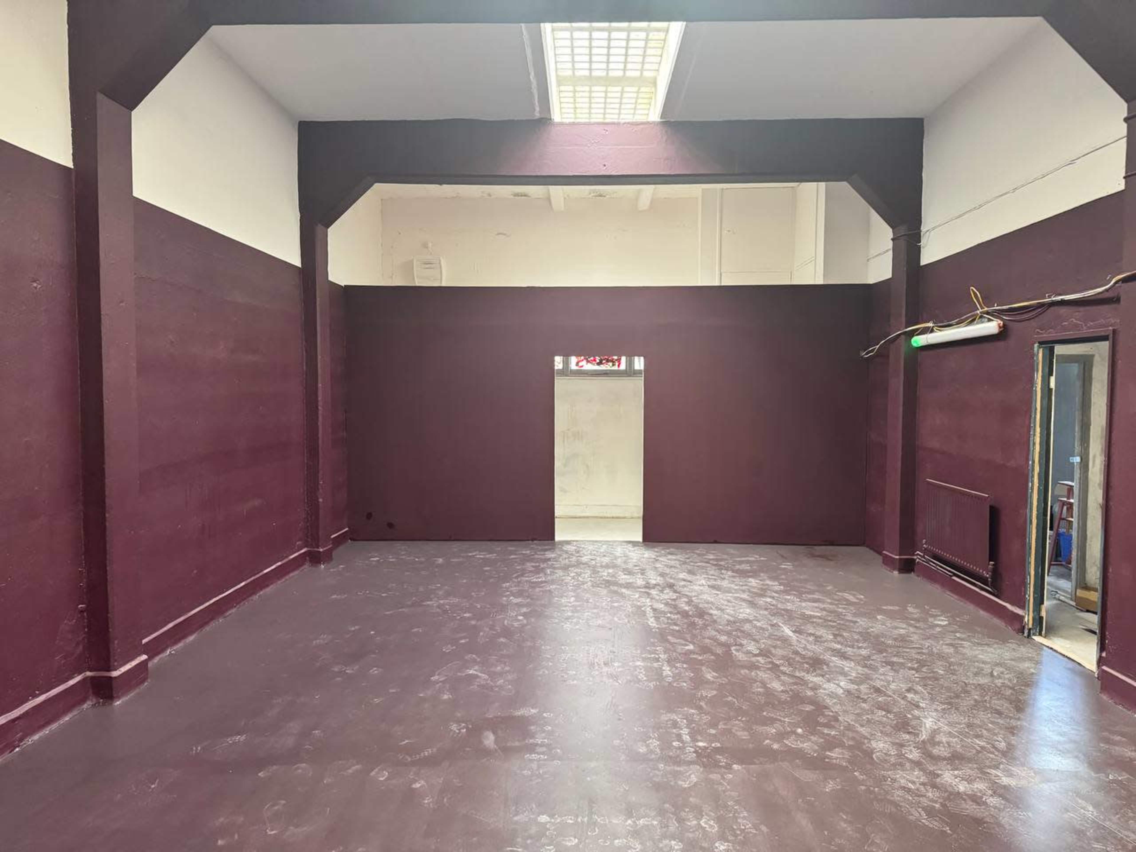 The image shows an empty room with maroon walls and a polished floor, featuring a doorway at the far end.