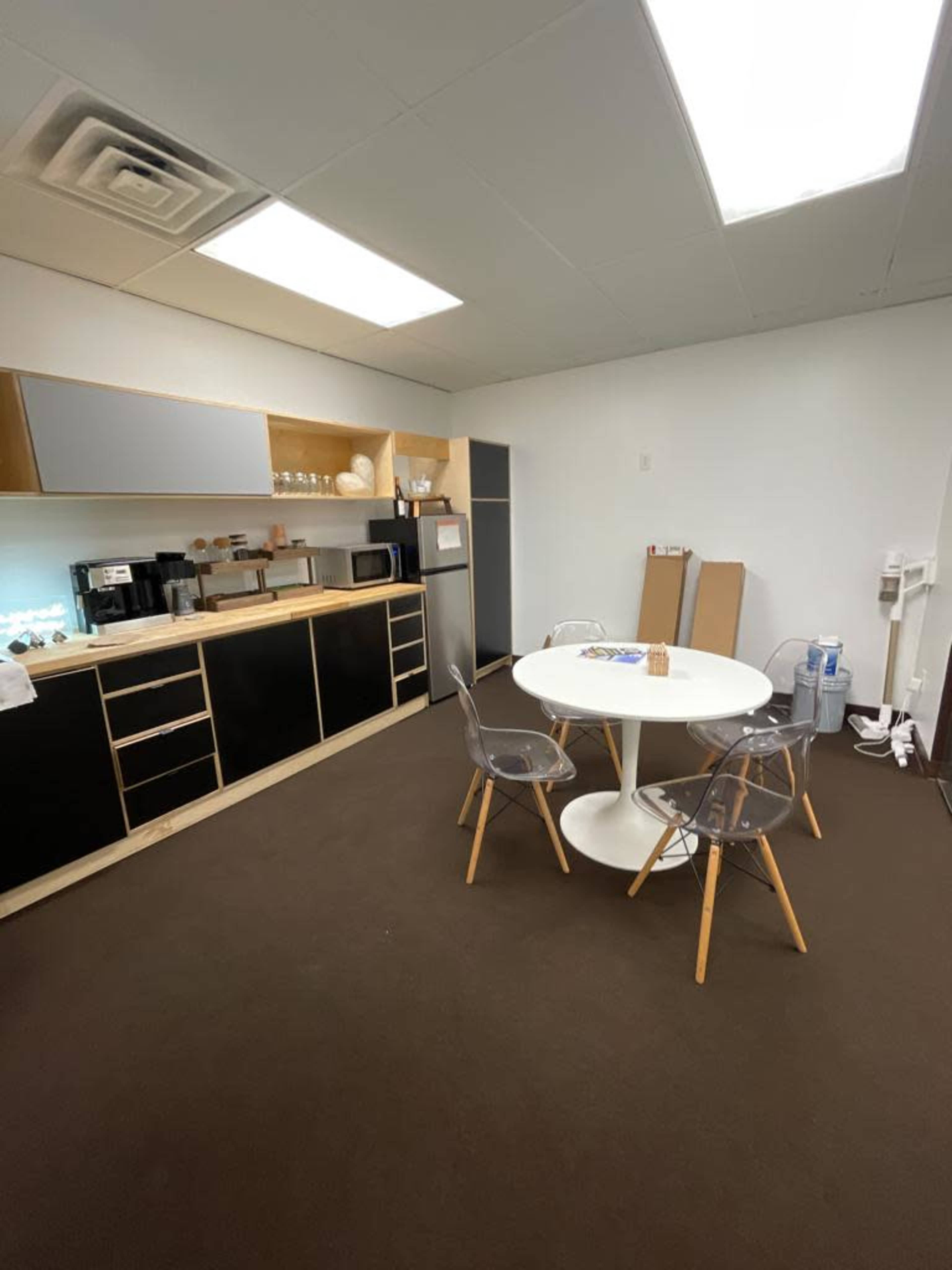 A modern kitchen area with a circular table and four chairs, along with cabinets, a refrigerator, and a coffee maker on the countertop.