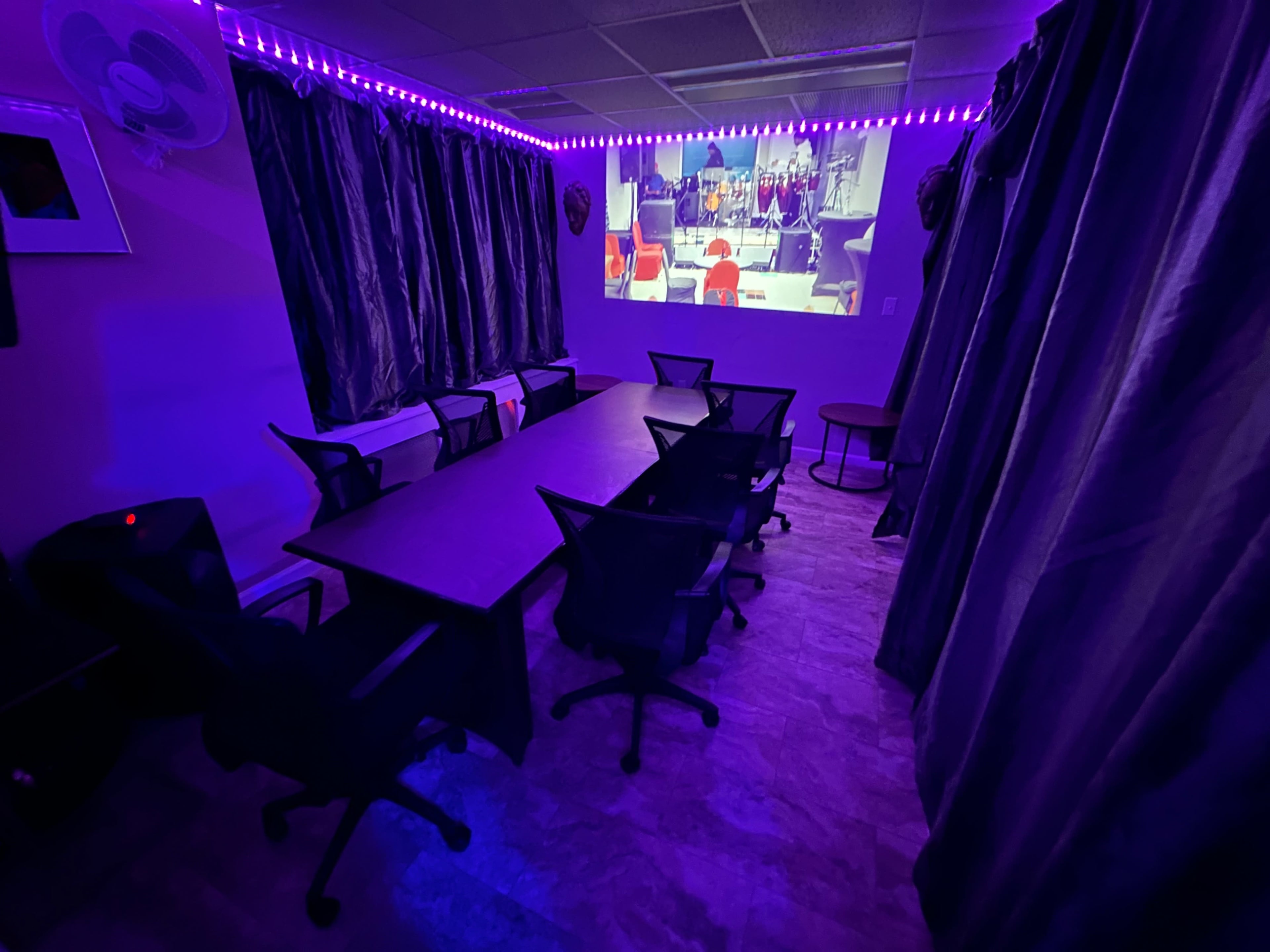 A dimly lit meeting room features a large table surrounded by chairs, with purple lighting and a projection screen displaying an event.