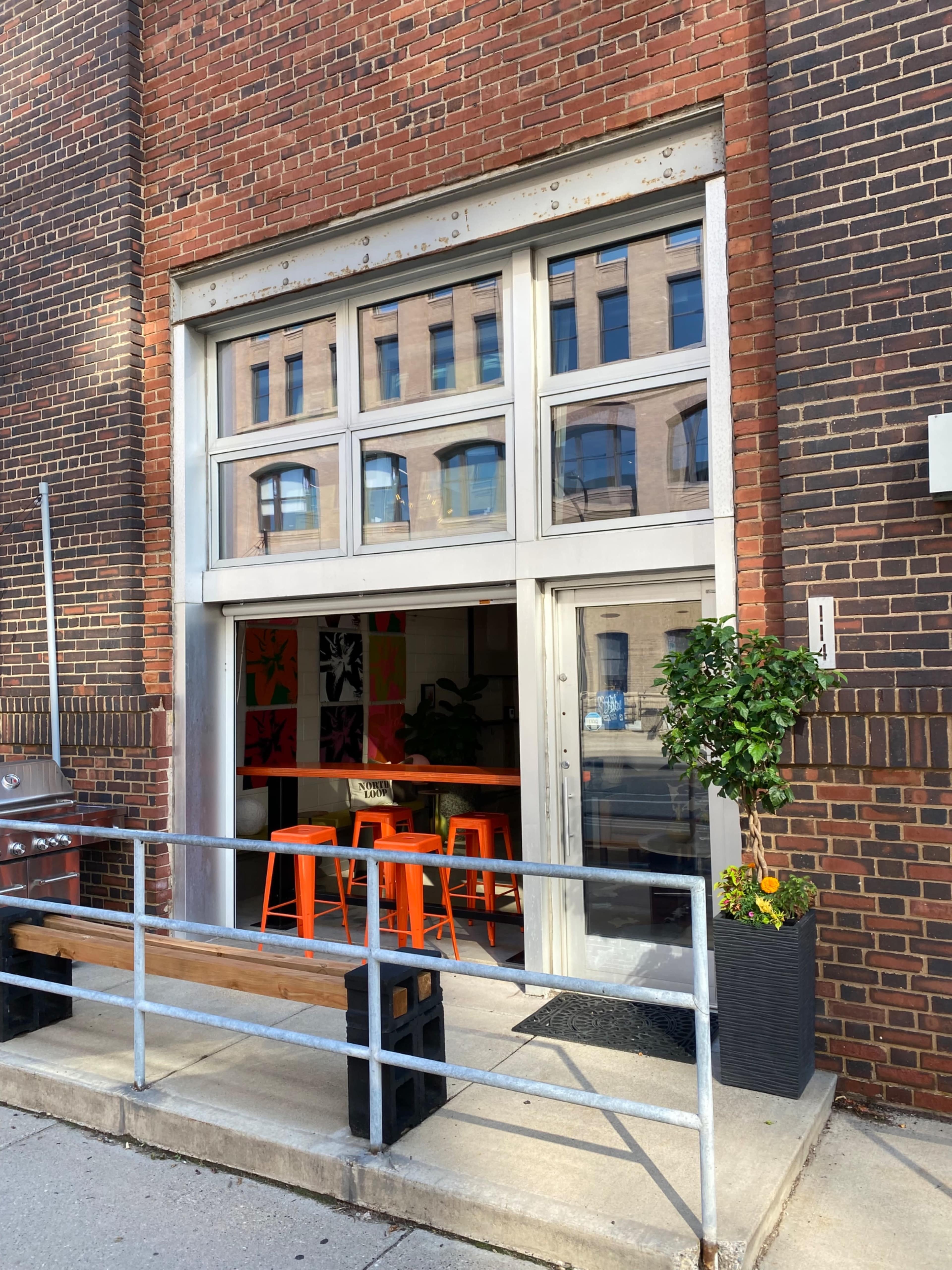 A large storefront with glass doors and a metal railing, featuring orange bar stools visible inside.