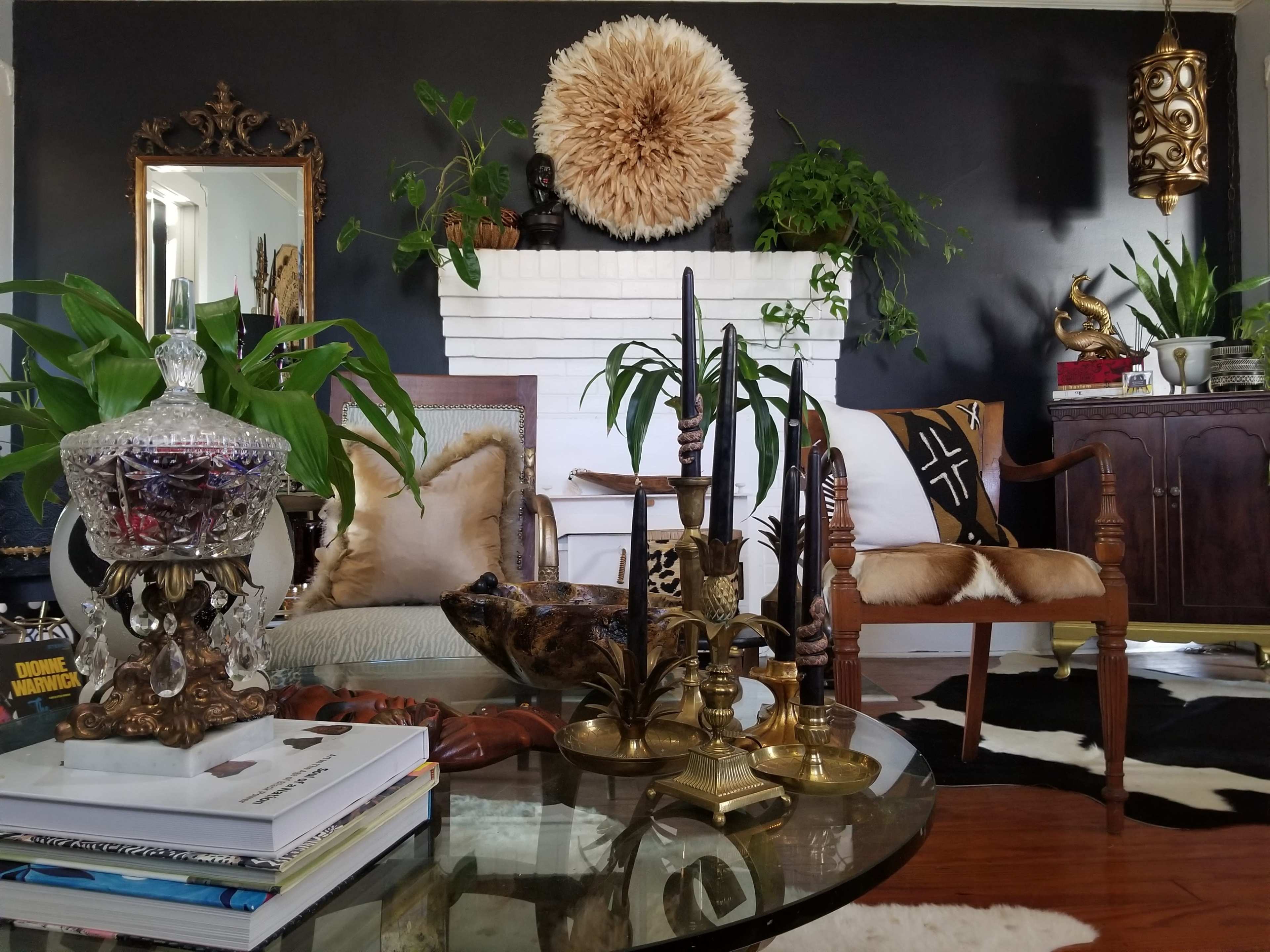 The living room features a mix of plants and decorative items, with a prominent black wall, a white fireplace, and various seating arrangements.