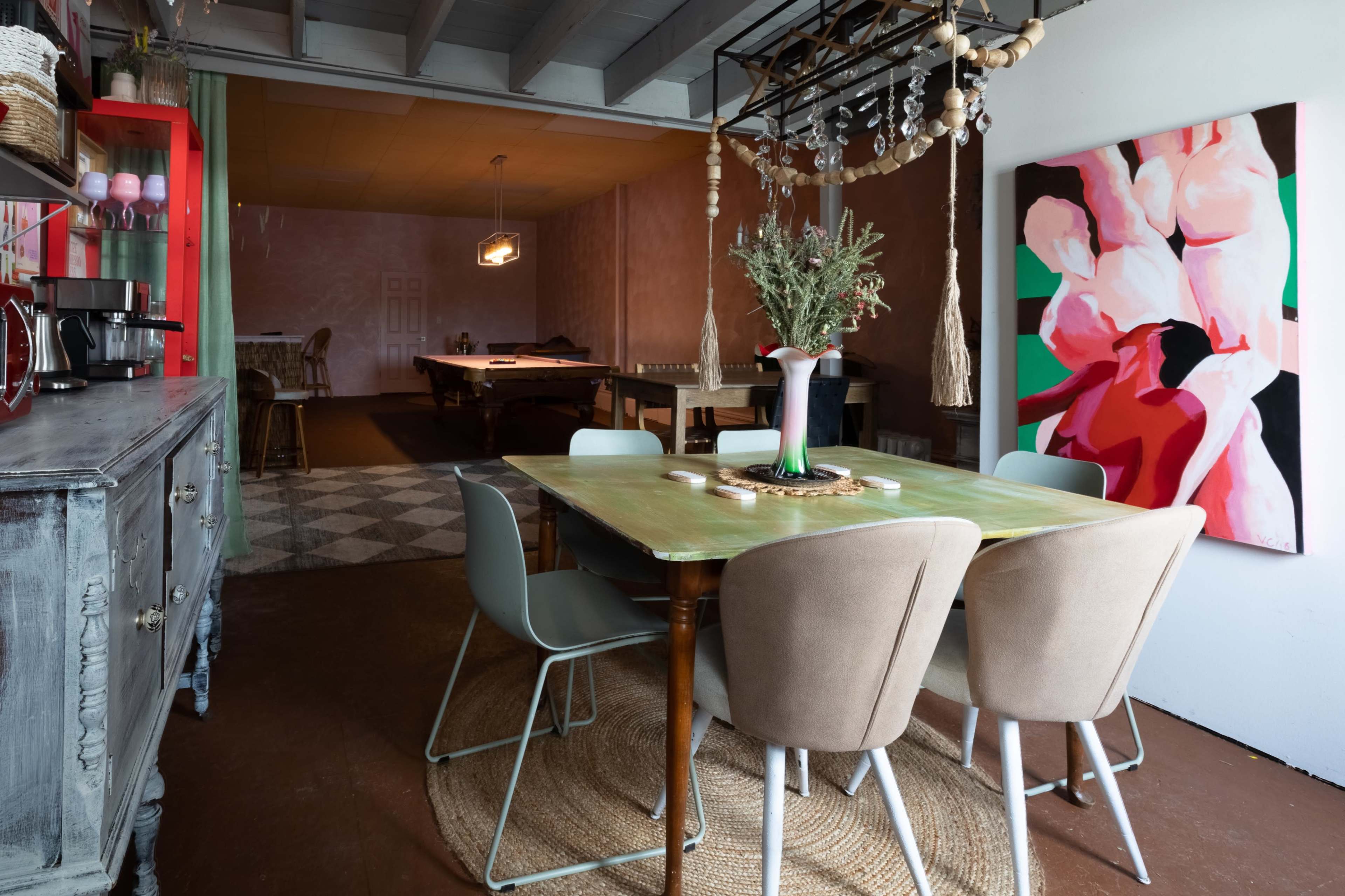 A dining area features a table surrounded by chairs, with a vase of flowers on the table and an abstract painting on the wall.