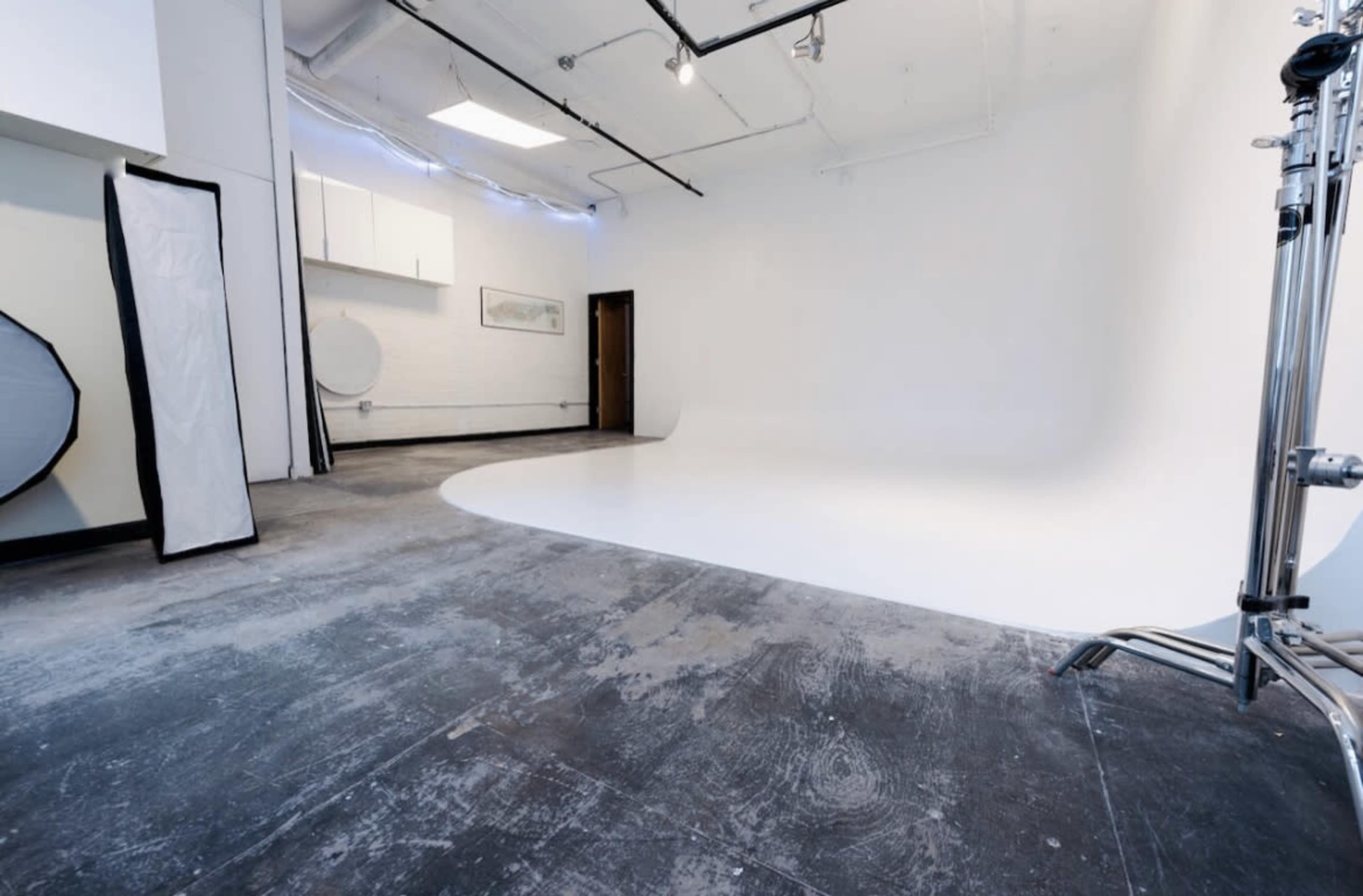 A spacious photo studio with a large white backdrop and concrete flooring.