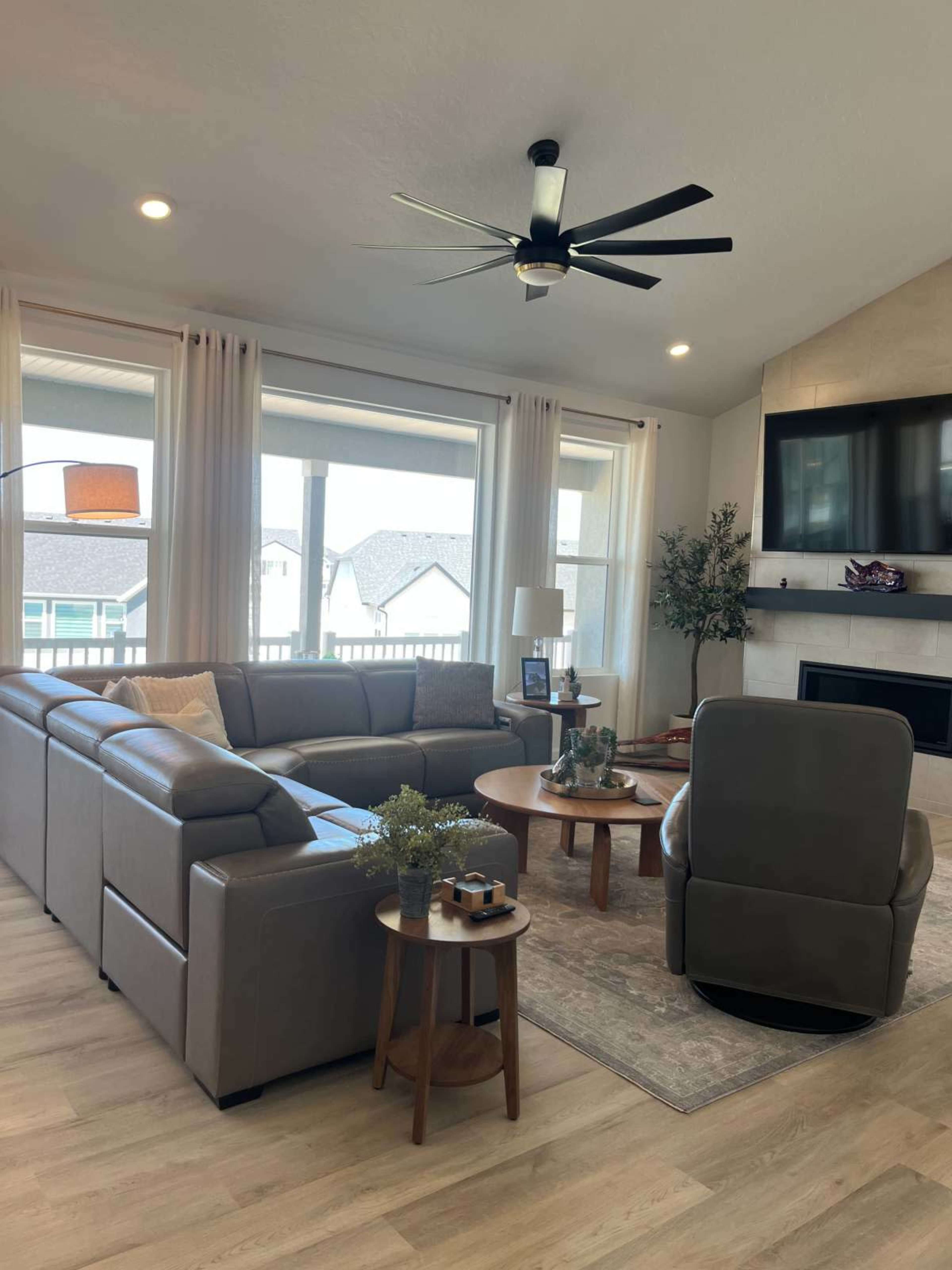 The living room features a sectional sofa, a round coffee table, and a comfortable armchair, with large windows allowing natural light to fill the space.
