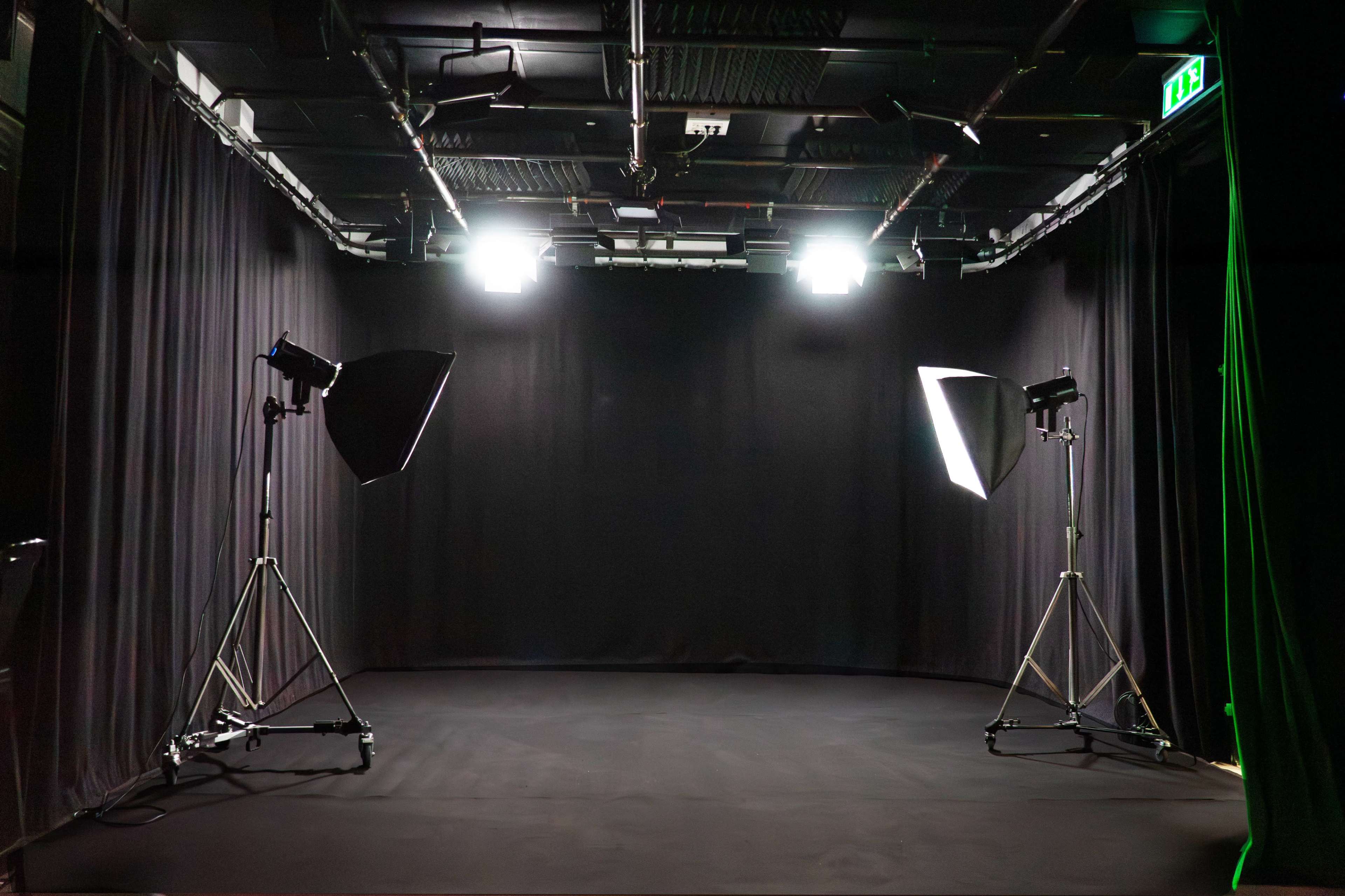 The image shows a dimly lit studio space with two lighting setups positioned on either side, surrounded by black curtains.