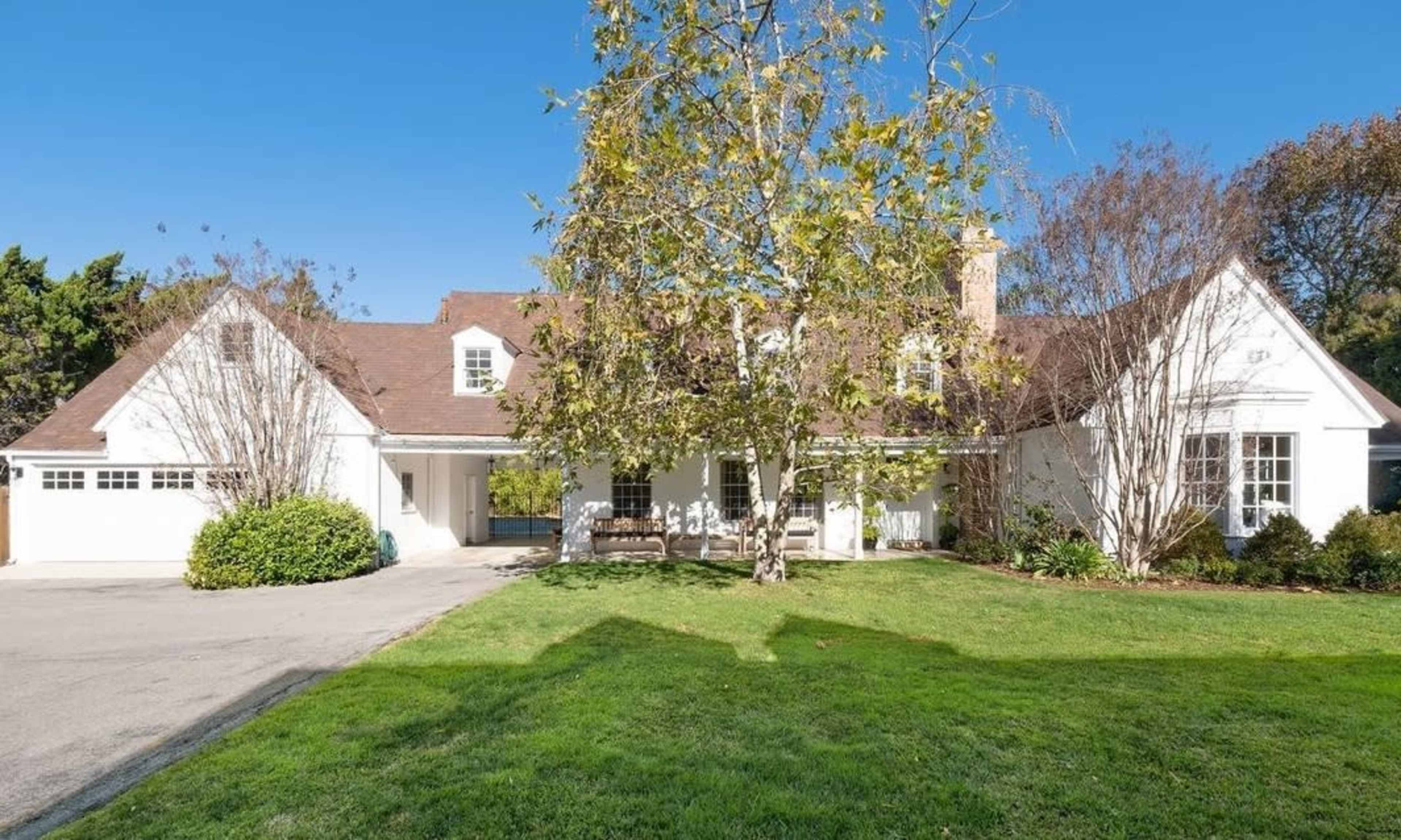 The image shows a large white house with a brown roof, a garage, and a lush green lawn in front.