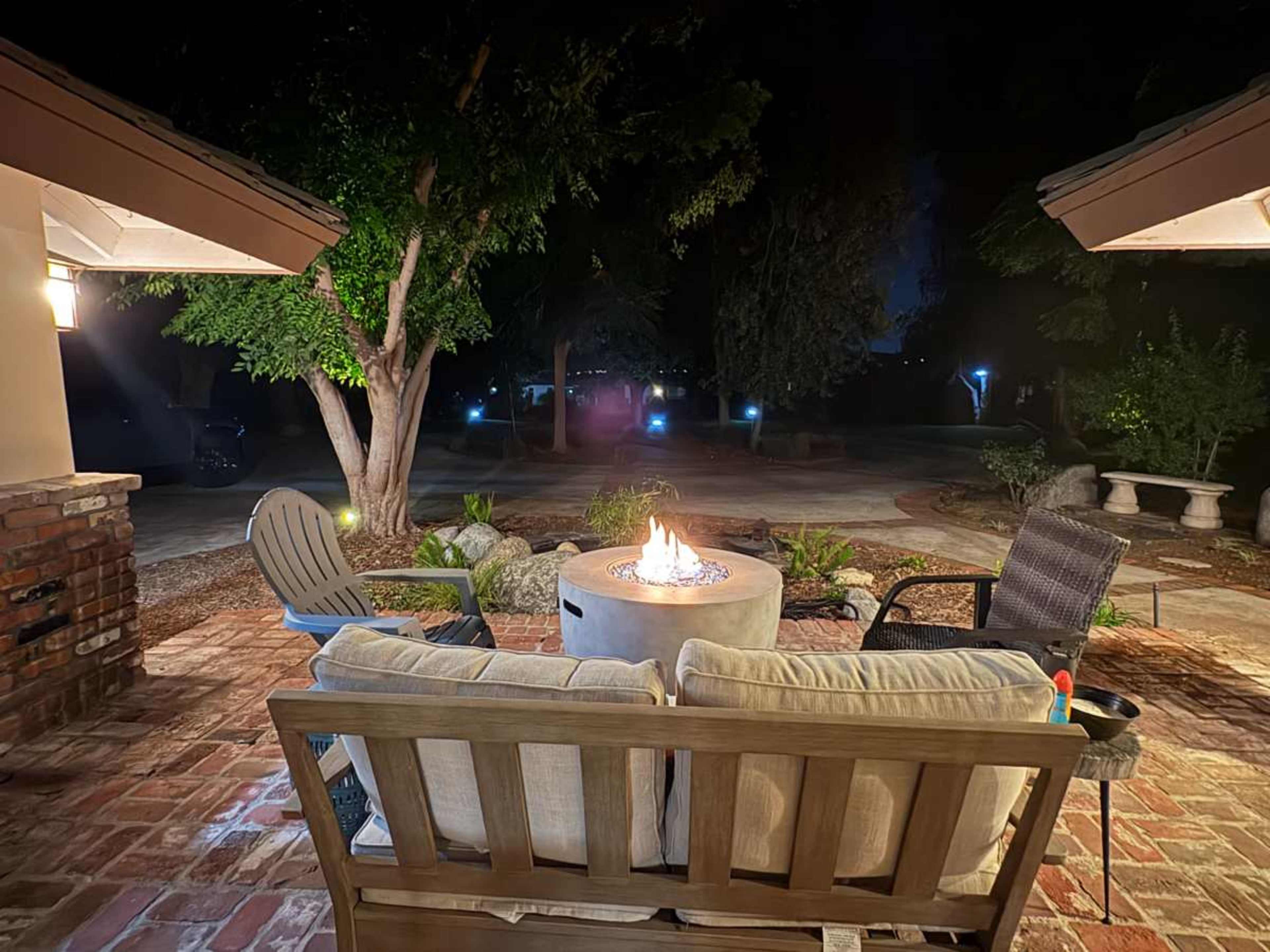 A cozy outdoor seating area features a fire pit surrounded by armchairs and a sofa under the night sky.