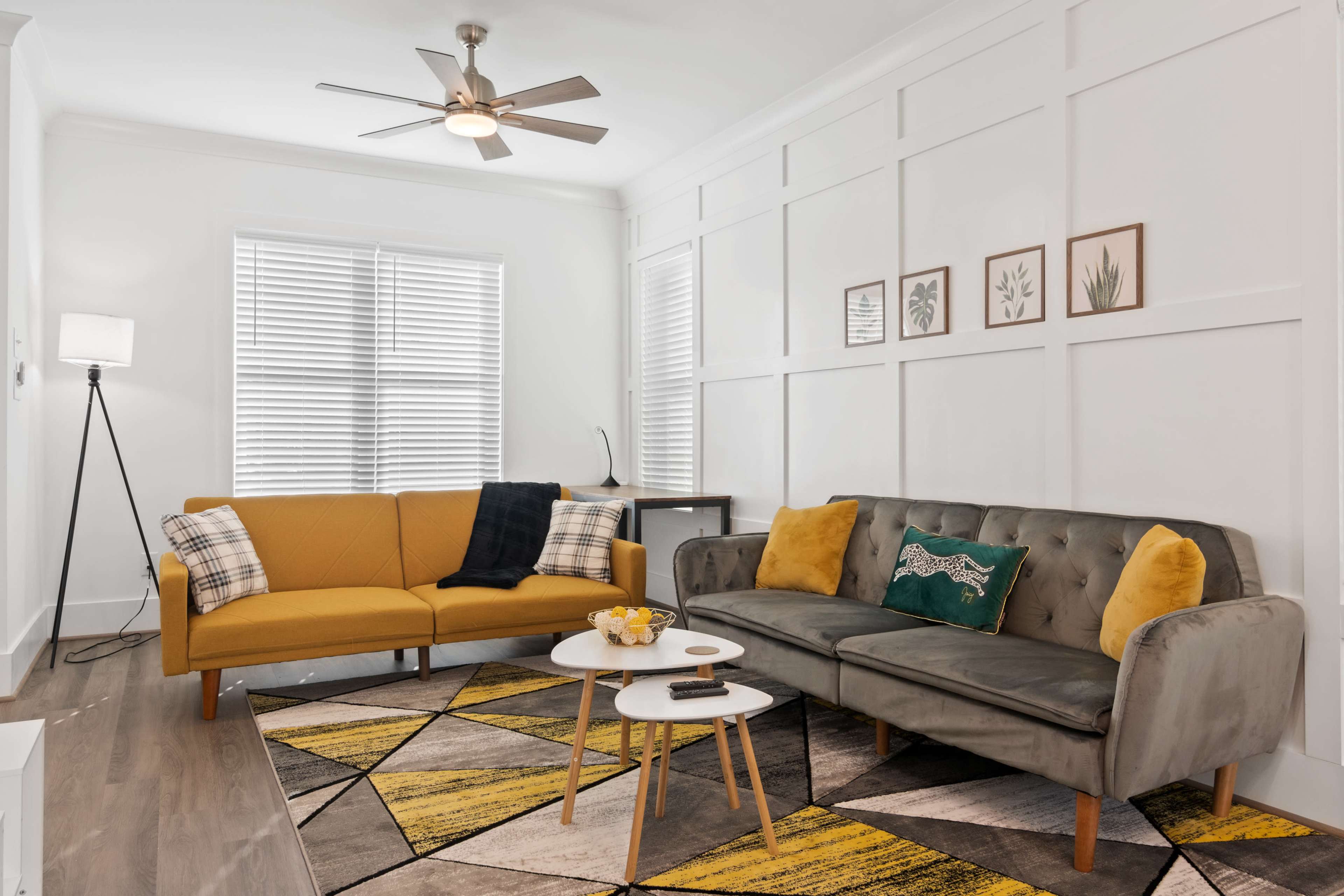 A modern living room featuring two sofas, one yellow and one gray, complemented by a geometric patterned rug and a small coffee table.