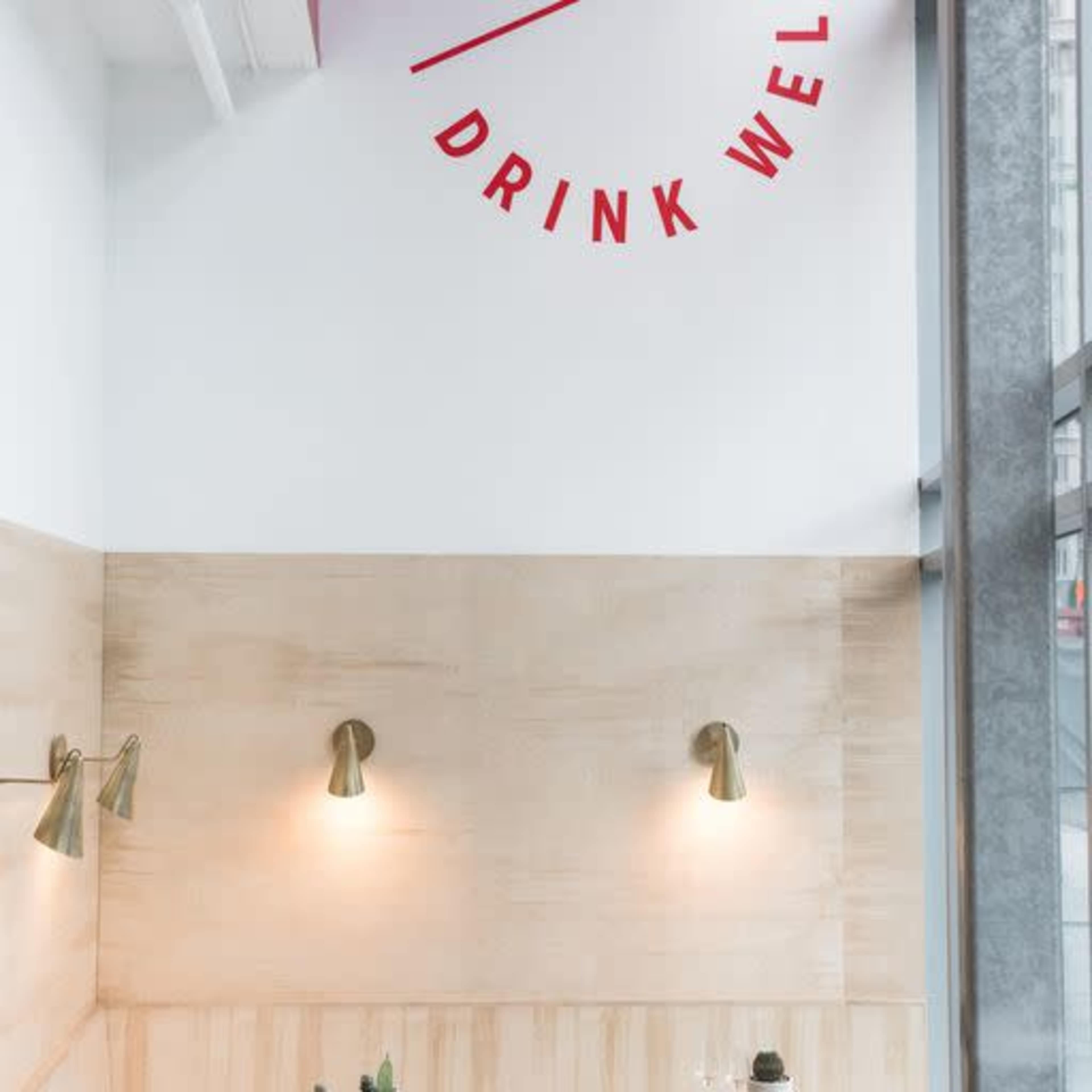 A wall with light wooden paneling featuring a circular red sign that says "DRINK WELL."