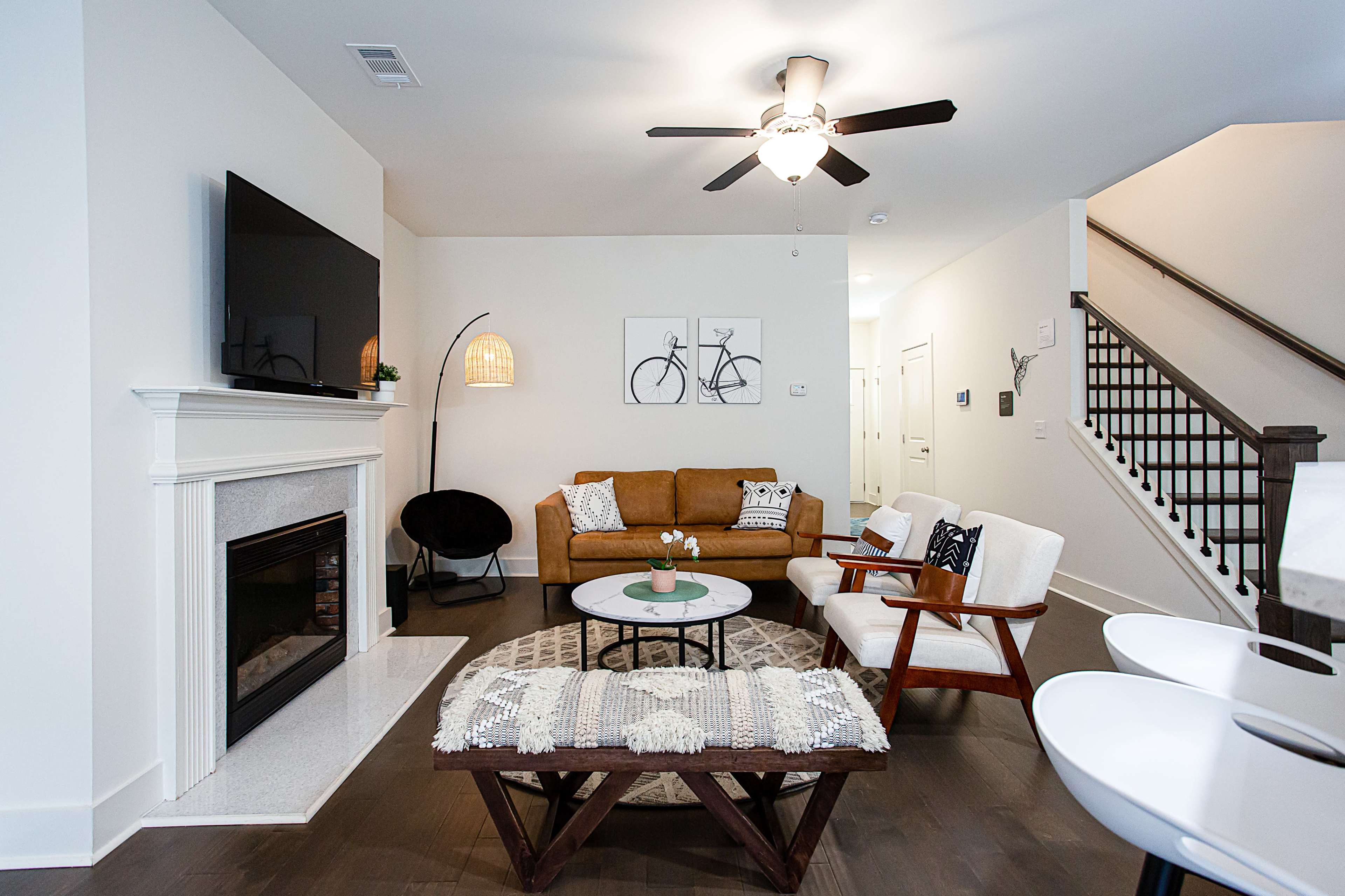 A modern living room with a brown sofa, white chairs, a round coffee table, and a wall-mounted television above a fireplace.