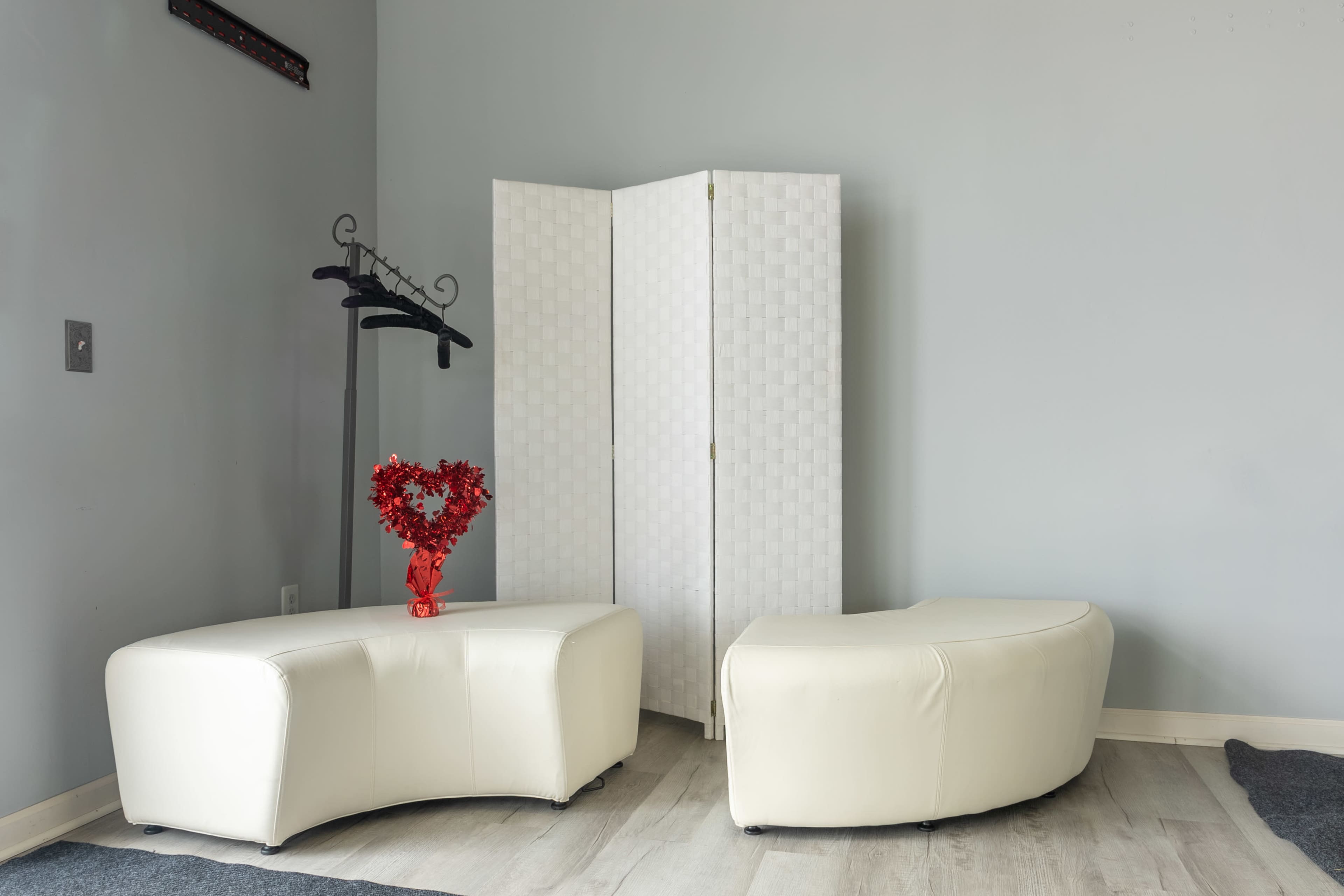 A minimalist room featuring two white curved sofas, a red heart-shaped decoration on a table, and a folding screen.