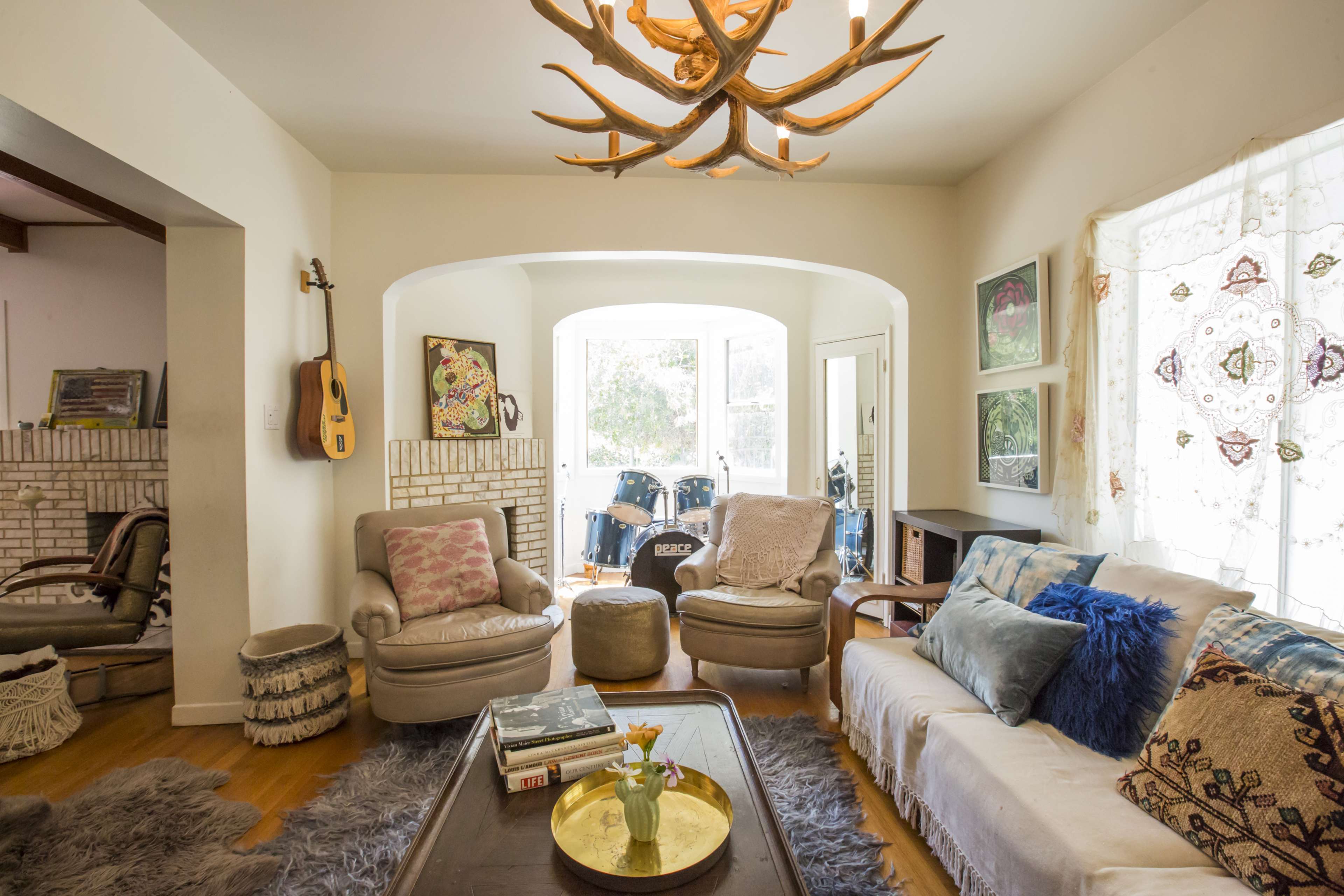 A cozy living room features a large window, comfortable seating, and a decorative antler chandelier.