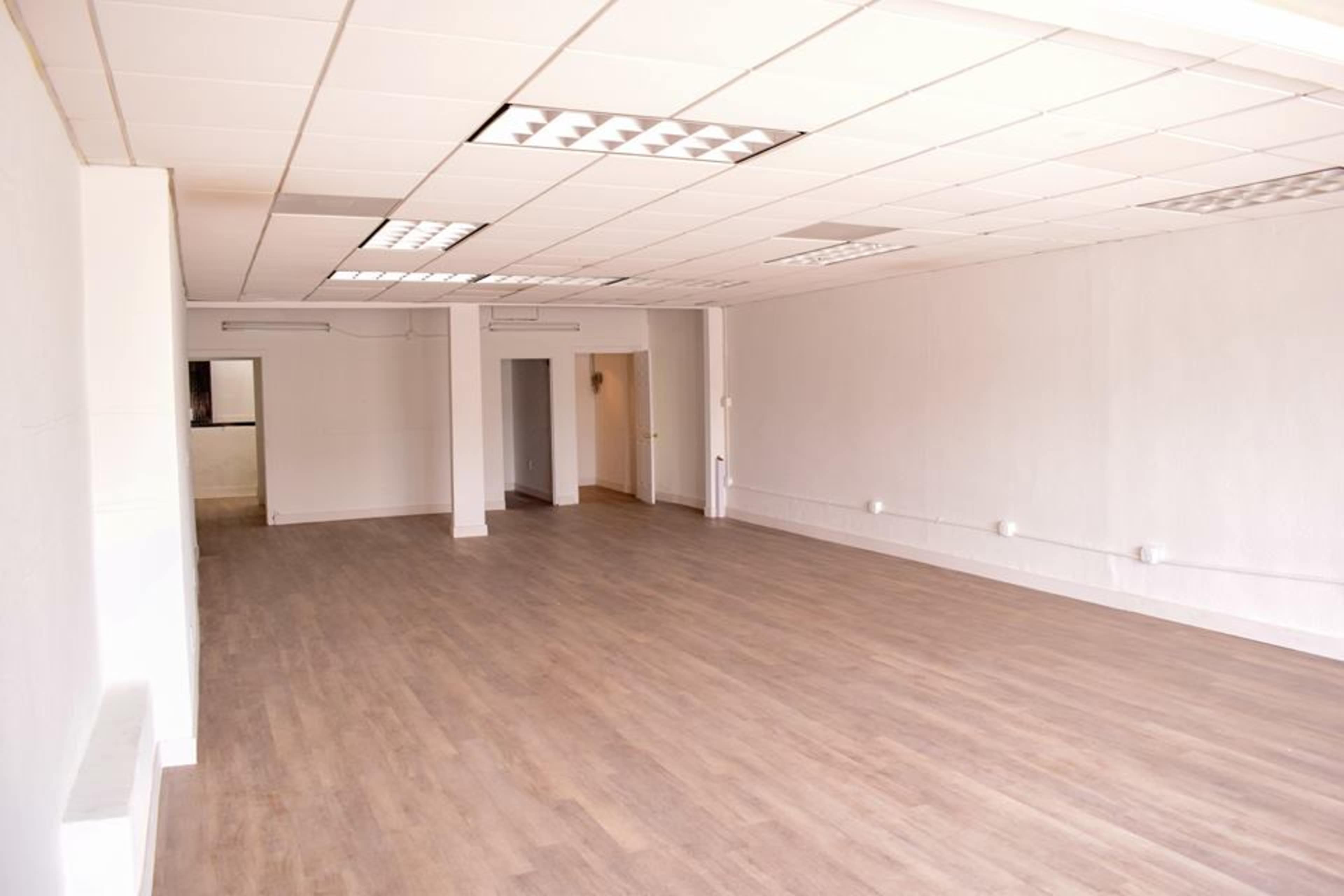 The image shows a vacant room with wooden flooring, white walls, and recessed ceiling lights.