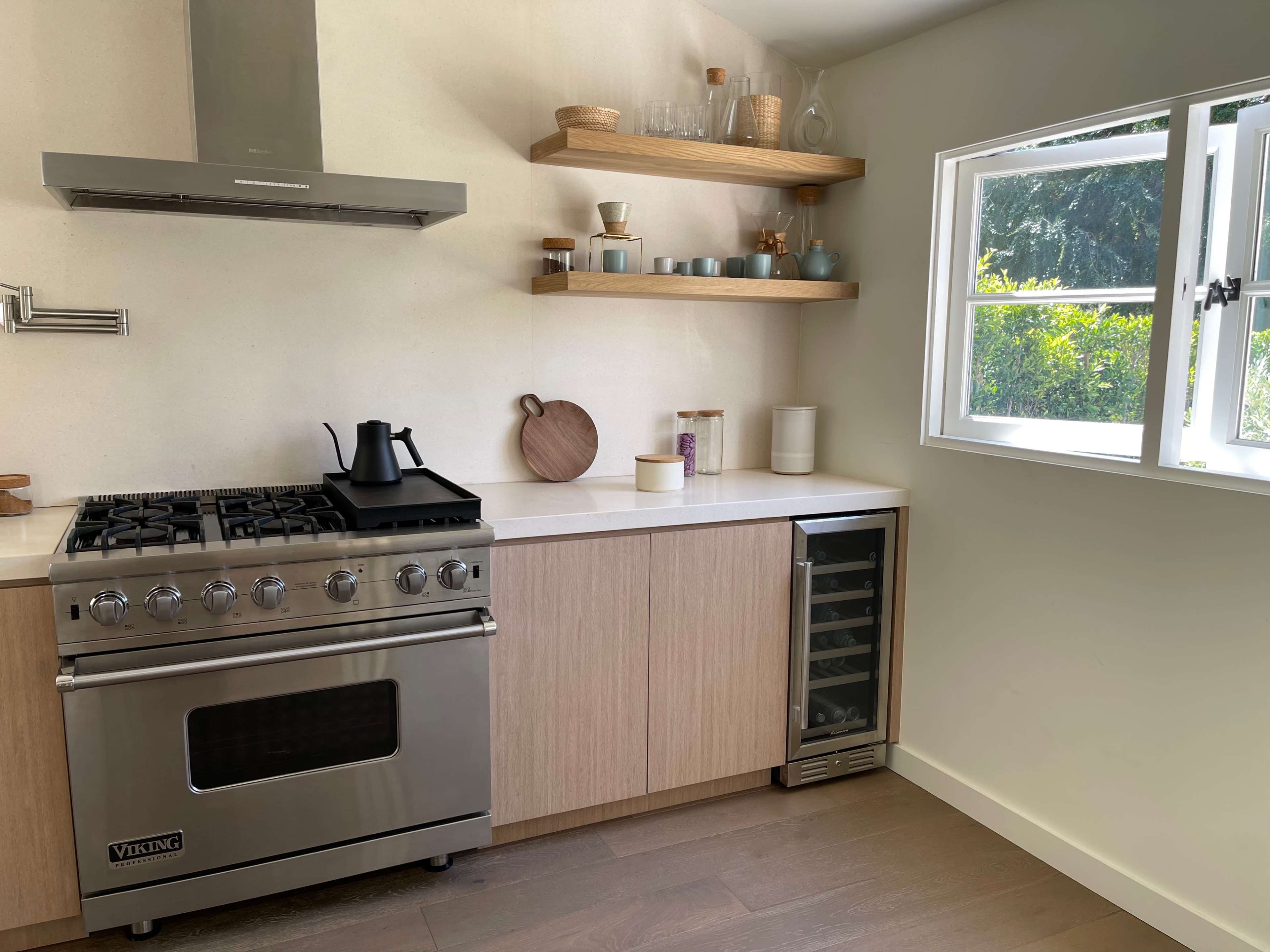 A modern kitchen features a stainless steel gas stove, wooden cabinetry, and open shelves displaying various kitchenware.