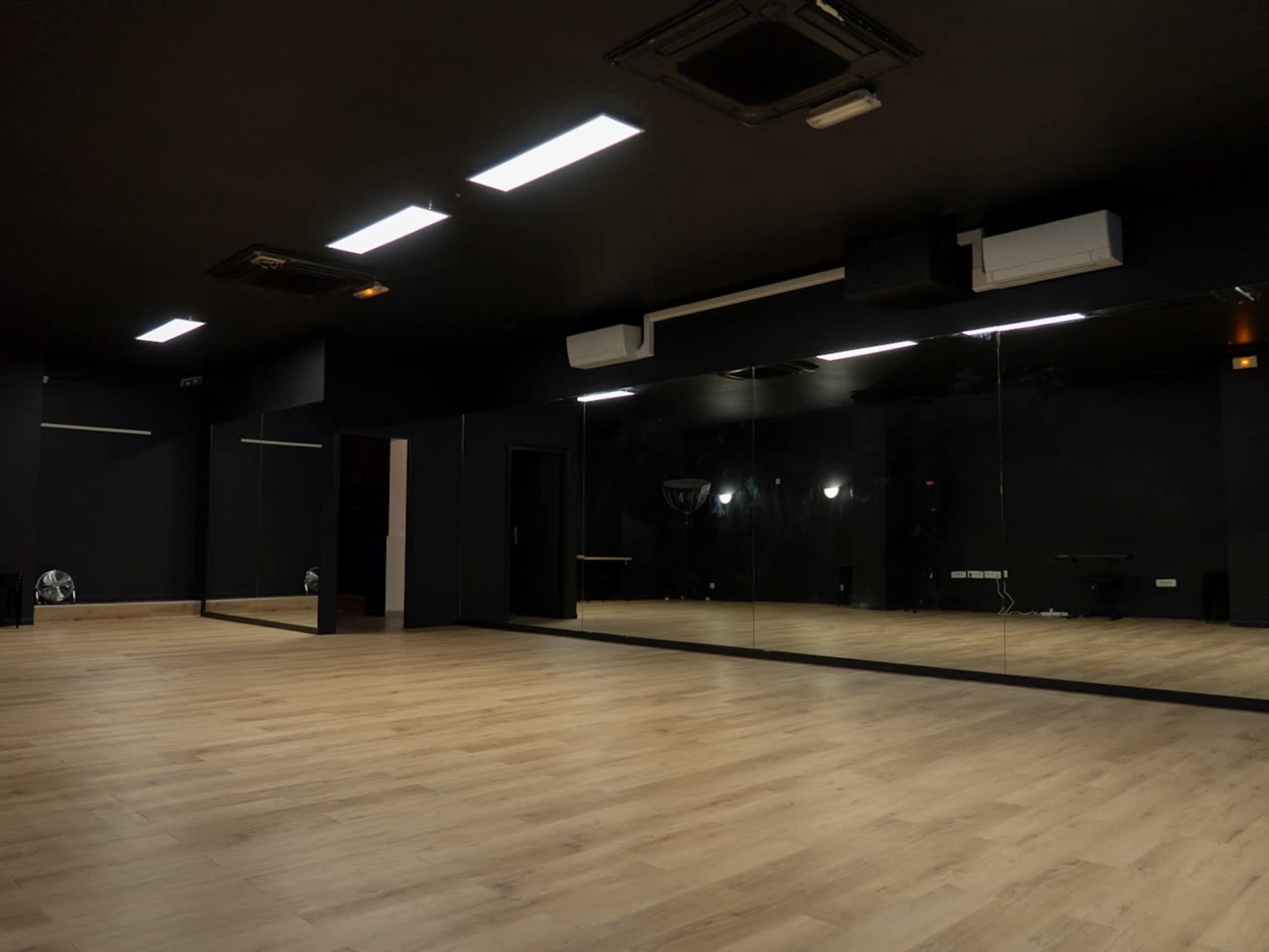 The image shows a spacious, dark-colored dance studio with wooden flooring and large mirrors on one wall.