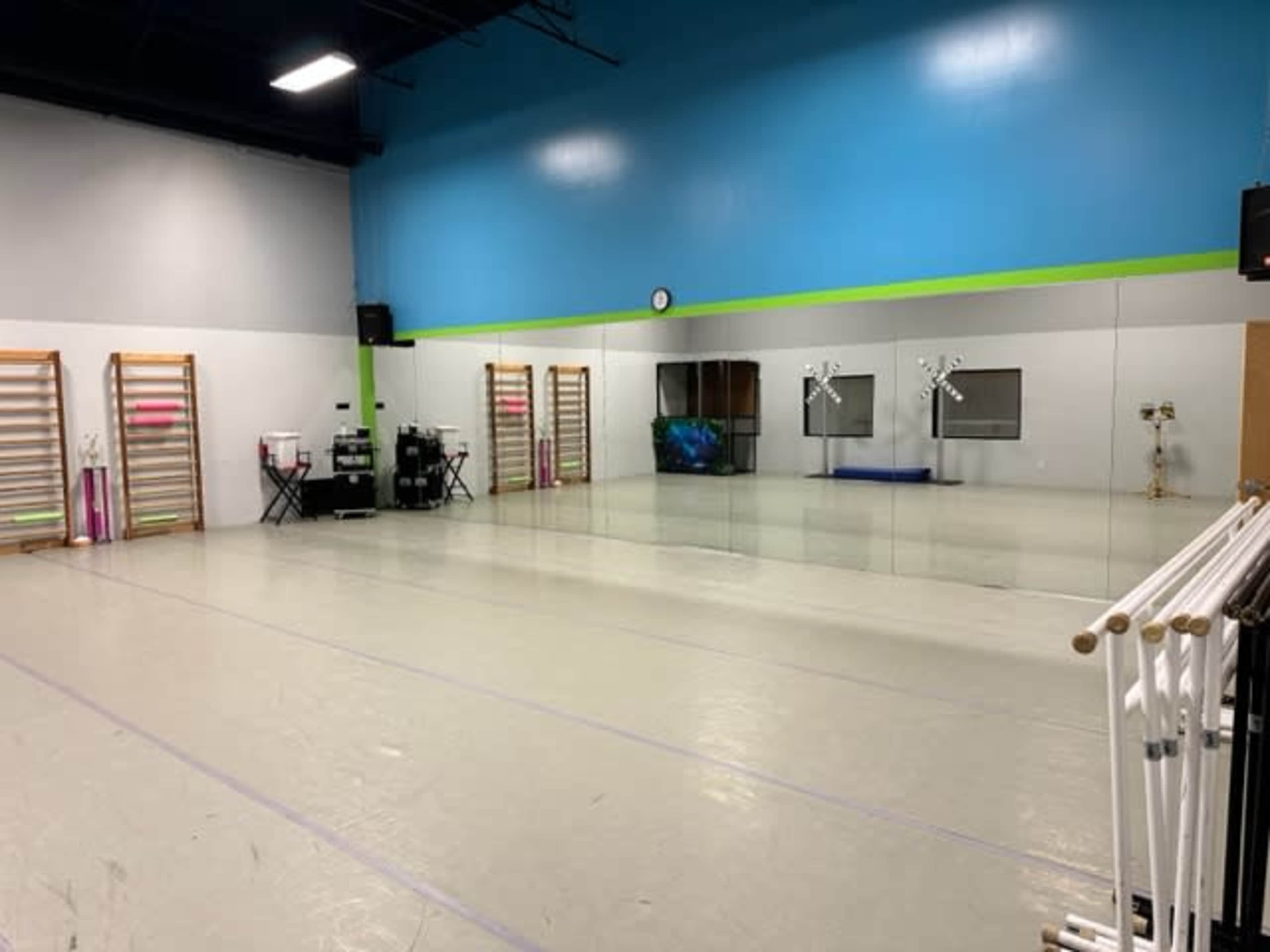 A spacious dance studio with mirrors on one wall, wooden ballet barres on the side, and exercise equipment against a brightly colored wall.