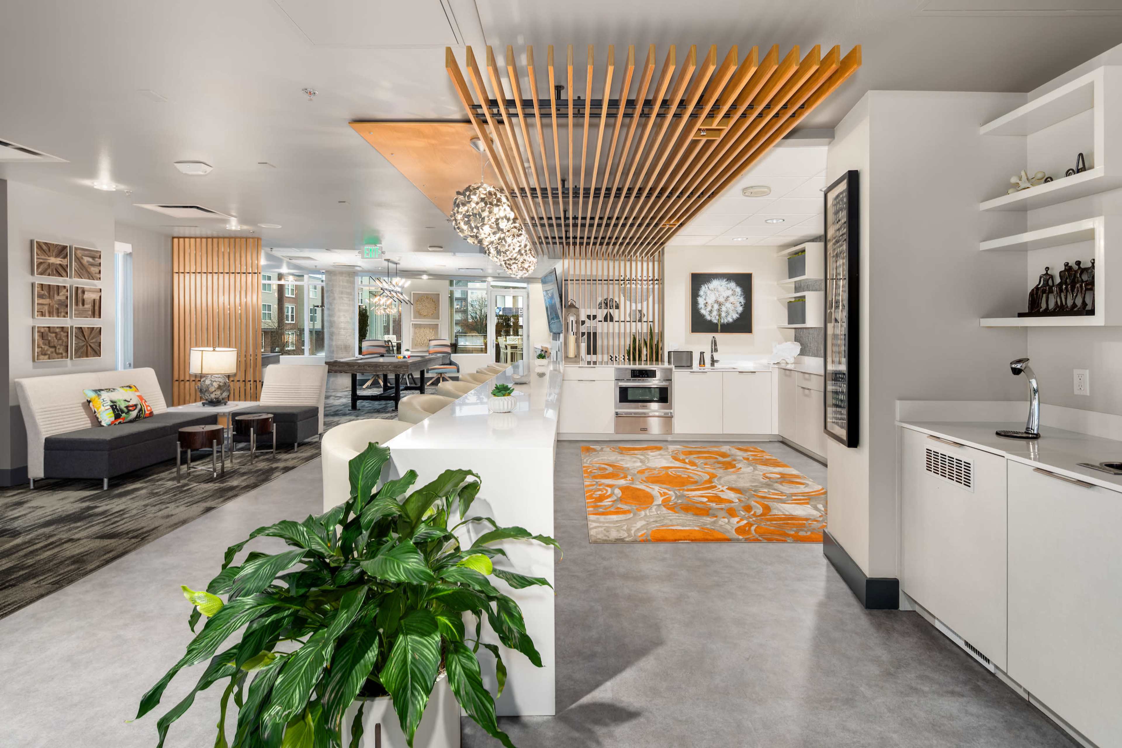 A modern open-concept living space featuring a kitchen with wooden accents, a dining area with an orange rug, and a lounge area with seating.