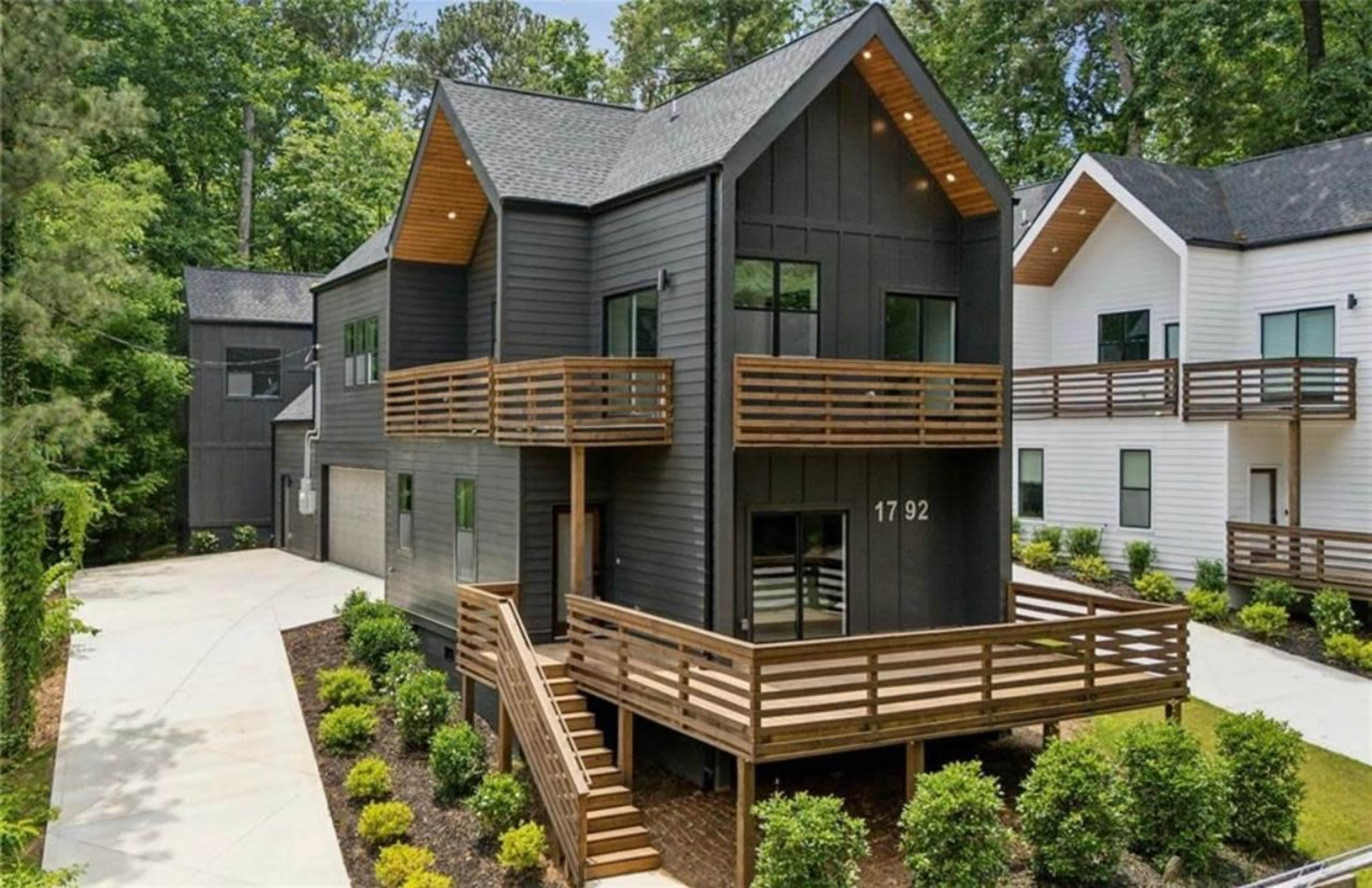 The image shows a modern two-story black wooden house with multiple balconies, surrounded by lush greenery.