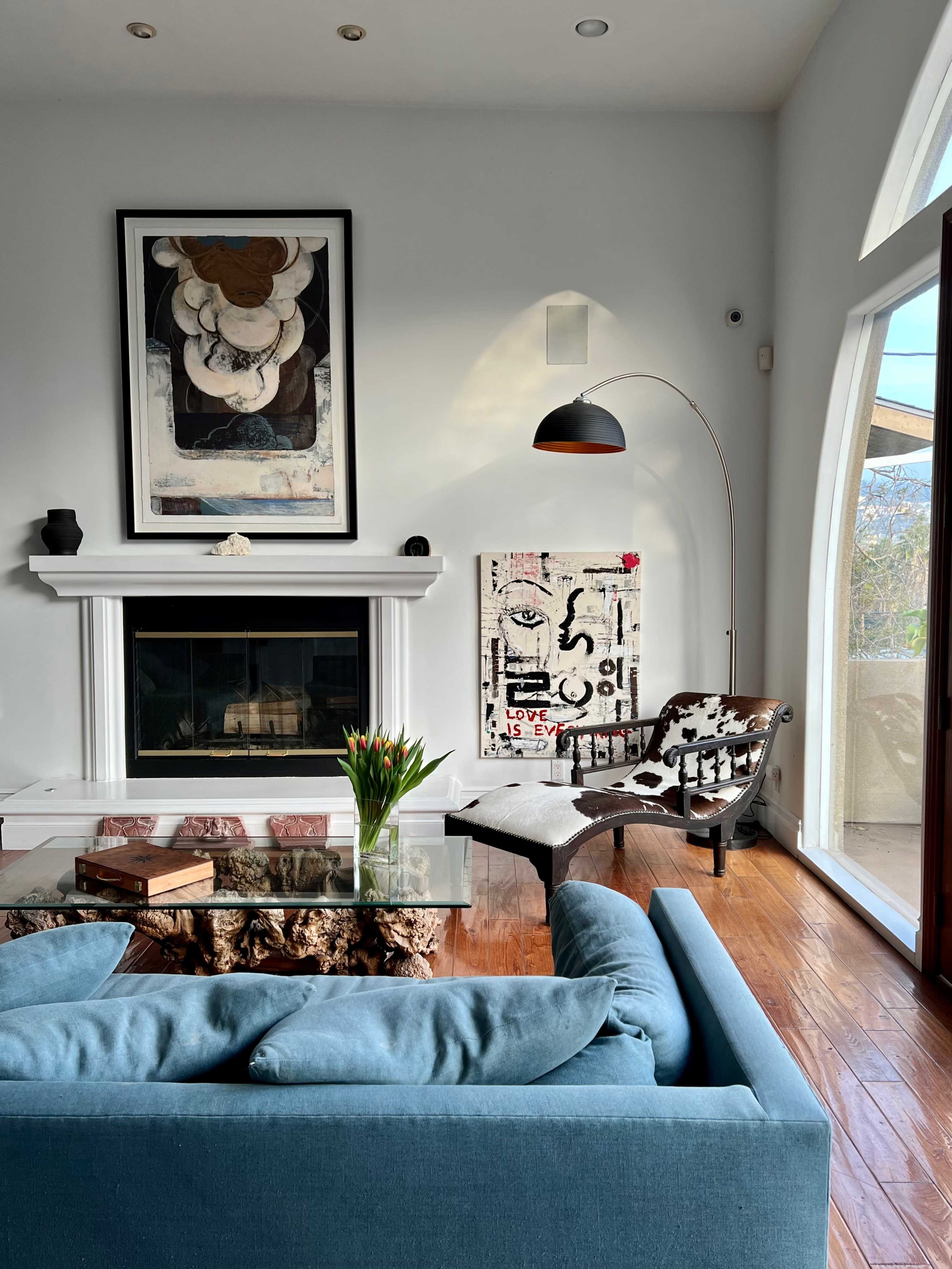 A modern living room with a blue sofa, a fireplace, an arc floor lamp, and a large piece of abstract artwork on the wall.