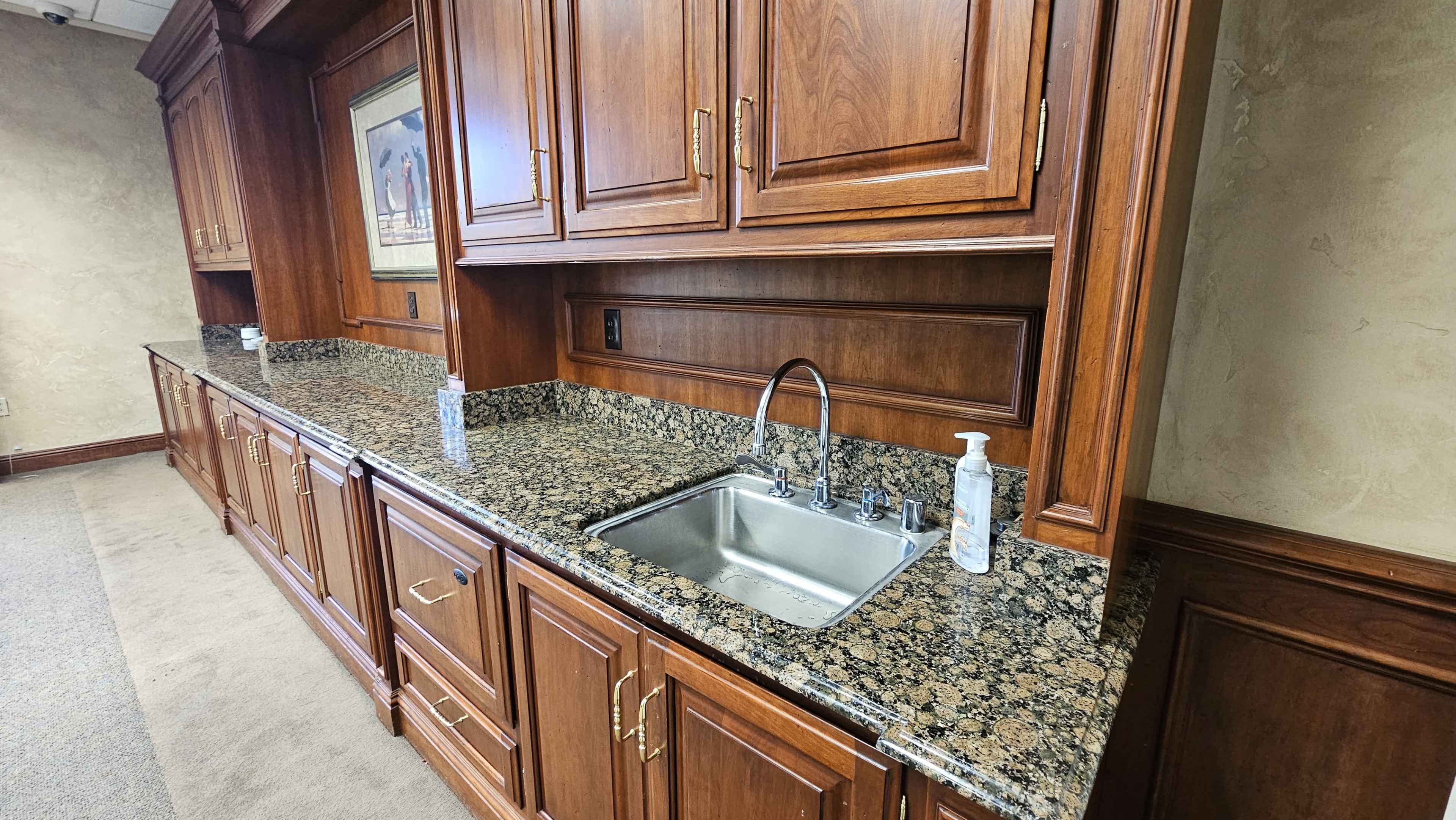 The image shows a wooden cabinetry area with a granite countertop and a small sink, flanked by dispensers of hand sanitizer.