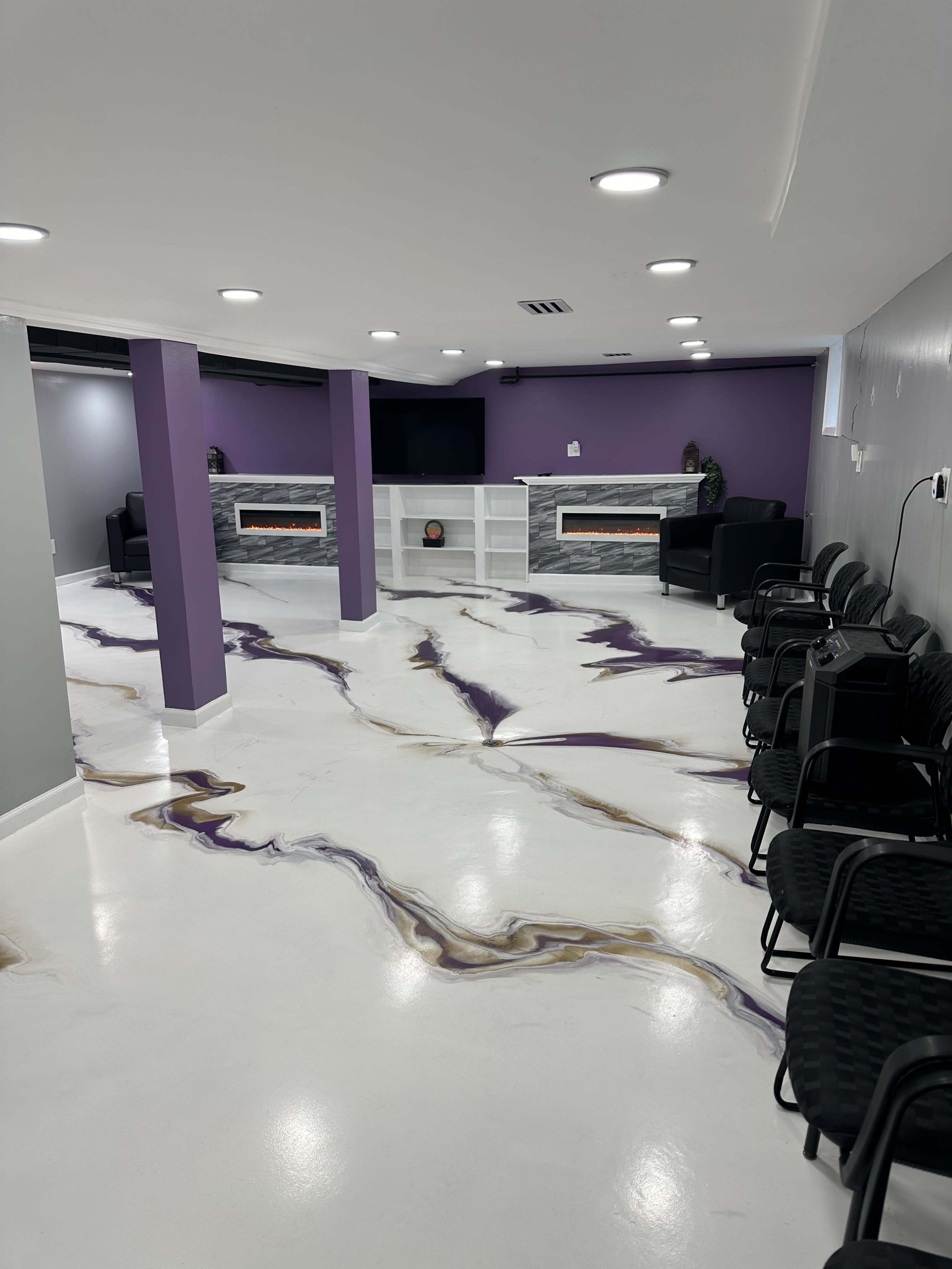 A modern interior space with a white floor featuring a marbled design in purple and gold, a seating area with black chairs, and a white entertainment unit against a purple wall.