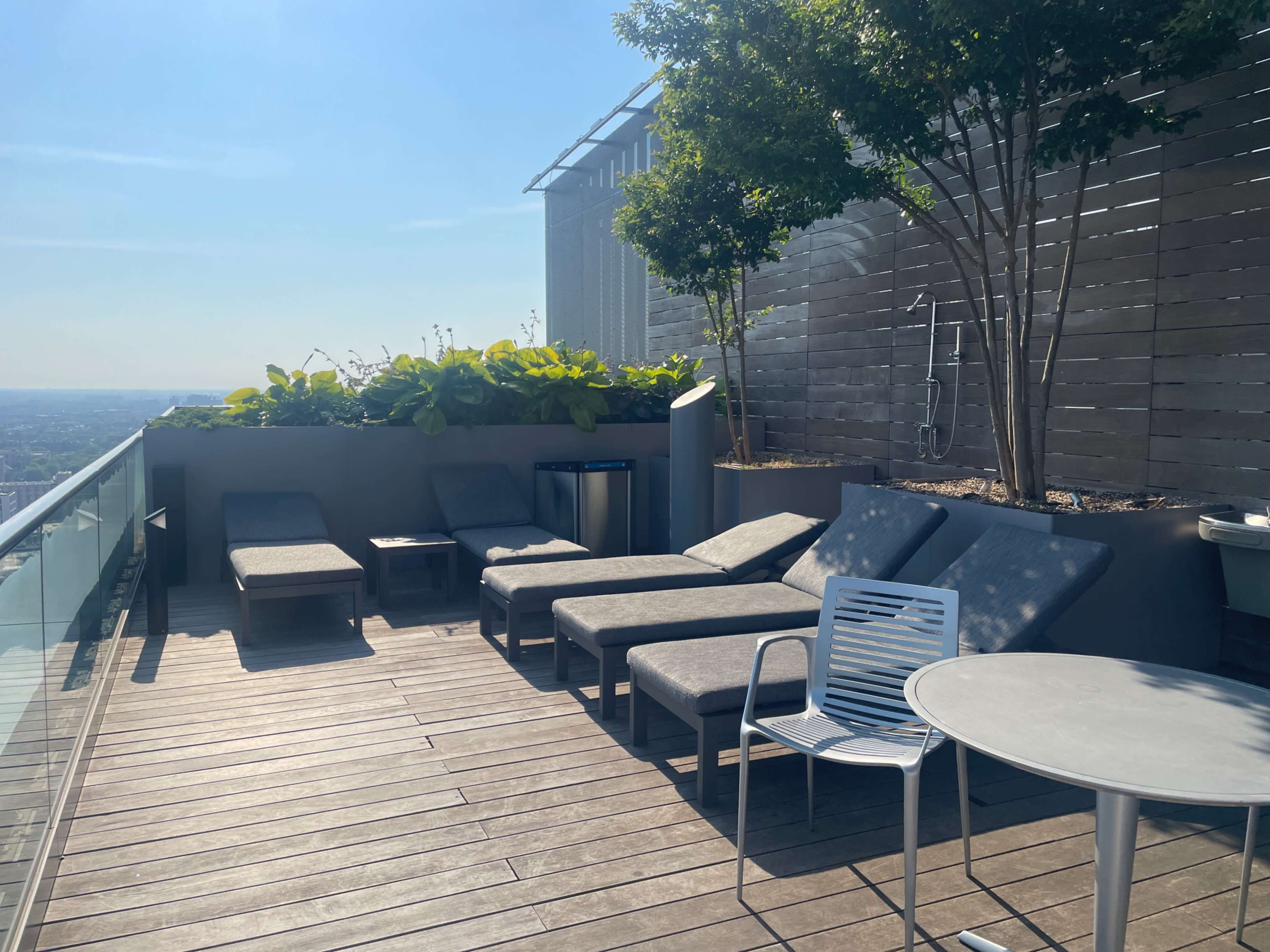 A rooftop terrace featuring lounge chairs, a small table, and a landscaped area with trees and plants.