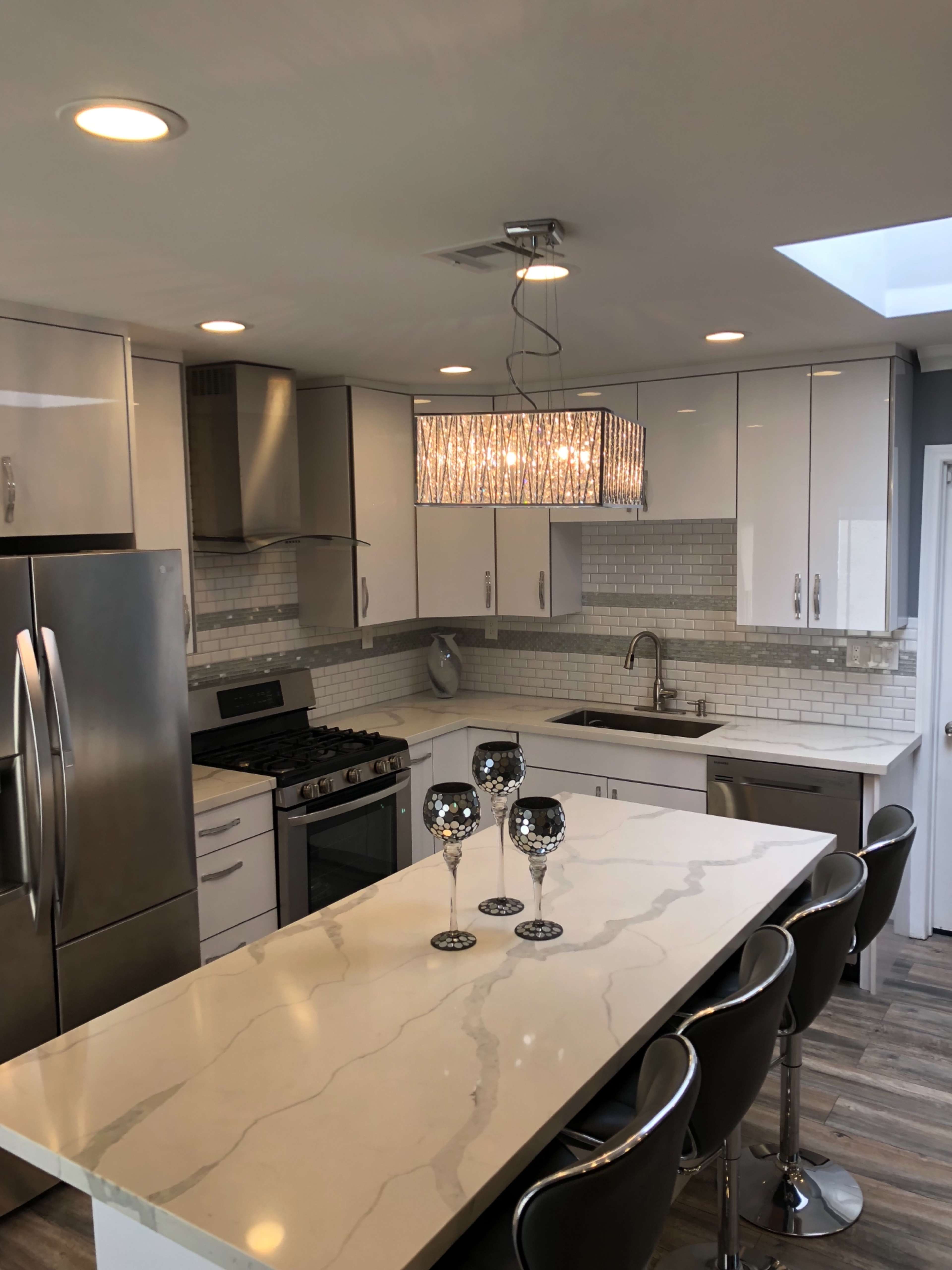 A modern kitchen featuring stainless steel appliances, a marble countertop island with bar stool seating, and a chandelier above.