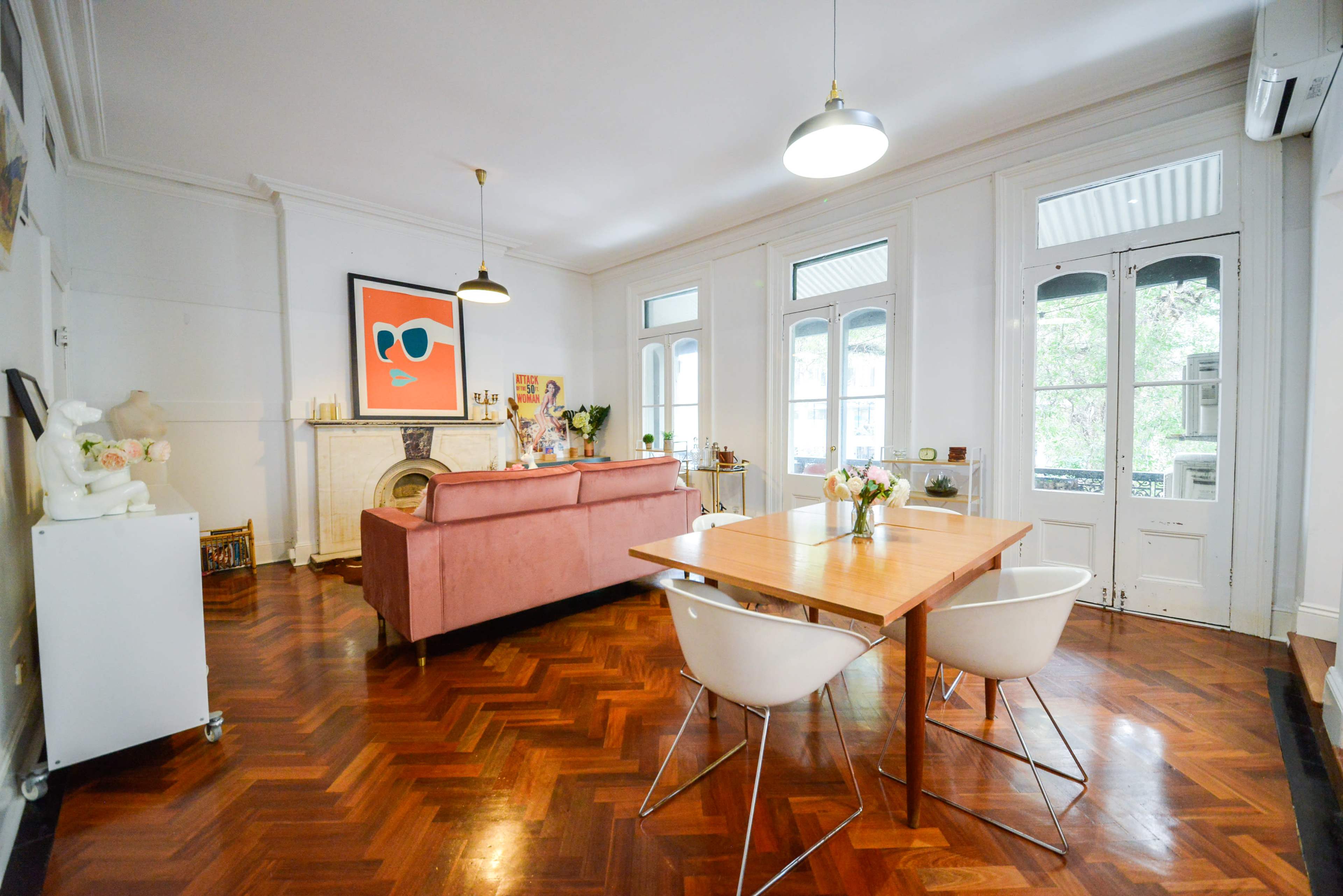 A modern living space featuring a pink sofa, a wooden dining table with white chairs, and large windows allowing natural light to enter.